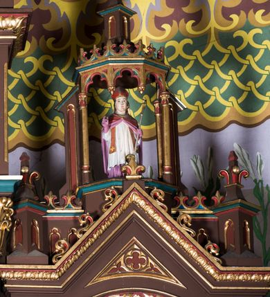 Zdjęcie nr 14: Ołtarz główny uzyskał formę architektonicznej struktury przyściennej, trójosiowej i jednokondygnacyjnej ze zwieńczeniem. Stipes ołtarzowy przyjął formę stołu, gdzie mensę z portatylem wsparto na czterech kolumnach ustawionych na wysokich wielobocznych bazach. Pomiędzy nimi usytuowano płaskorzeźbioną sceną Ostatniej Wieczerzy w kształcie leżącego prostokąta. Na mensie w osi ołtarza ustawione zostało tabernakulum z tronem wystawienia w kształcie baldachimu, stanowiące cześć środkową architektonicznego, trójosiowego założenia, gdzie w osiach bocznych w półokrągłych aediculach z wimpergami ustawiono parę adorujących aniołów. Nastawa ustawiona na wysokim cokole została dekorowana profilowanymi płycinami, ponad którymi poprowadzono profilowanym gzyms. Oś środkowa retabulum została ujęta złoconymi kolumnami o korynckich kapitelach i gładkich trzonach. Kolumny dźwigają półkoliście zamkniętą arkadę zwieńczoną profilowanym gzymsem z trójkątnie zakończoną wimpergą ozdobioną żabkami. Zwieńczenie utworzono w formie ażurowej kapliczki na rzucie wieloboku mieszczącej pełnoplastyczną figurę Michała Archanioła trzymającego miecz i wagę. Kapliczkę zakończono wieloboczną fialą o ściankach zdobionych ślepymi maswerkami. W osiach skrajnych wykonano analogiczne arkady wsparte na złoconych kolumnach mieszczące figury św. Piotra (z lewej) i św. Pawła (z prawej). W zwieńczeniach w osi znalazły się w ażurowych kapliczkach zakończonych fialami pełnoplastyczne figury św. Wojciecha i św. Stanisława w strojach pontyfikalnych. W polu ołtarza usytuowano obraz przedstawiający wszystkich świętych adorujących Trójcę Przenajświętszą. Pole ujmuje płaskorzeźbiona, złocona rama z dekoracją akantową zamknięta łukiem trójlistnym. W podłuczu wykonano arkaturę. Na zasuwie umieszczono obraz Najświętszego Serca Pana Jezusa. W płycinach wypełniających elementy architektoniczne znalazła się stylizowana dekoracja akantowa oraz motyw czwórliścia wpisanego w okrąg. Struktura ołtarza została polichromowana w odcieniach zgaszonej czerwieni i złamanego brązu wchodzącego w fiolet. Ornamentyka oraz detale elementów i profilów architektonicznych wyzłocono.