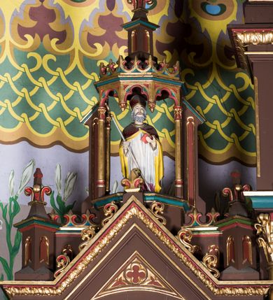 Zdjęcie nr 15: Ołtarz główny uzyskał formę architektonicznej struktury przyściennej, trójosiowej i jednokondygnacyjnej ze zwieńczeniem. Stipes ołtarzowy przyjął formę stołu, gdzie mensę z portatylem wsparto na czterech kolumnach ustawionych na wysokich wielobocznych bazach. Pomiędzy nimi usytuowano płaskorzeźbioną sceną Ostatniej Wieczerzy w kształcie leżącego prostokąta. Na mensie w osi ołtarza ustawione zostało tabernakulum z tronem wystawienia w kształcie baldachimu, stanowiące cześć środkową architektonicznego, trójosiowego założenia, gdzie w osiach bocznych w półokrągłych aediculach z wimpergami ustawiono parę adorujących aniołów. Nastawa ustawiona na wysokim cokole została dekorowana profilowanymi płycinami, ponad którymi poprowadzono profilowanym gzyms. Oś środkowa retabulum została ujęta złoconymi kolumnami o korynckich kapitelach i gładkich trzonach. Kolumny dźwigają półkoliście zamkniętą arkadę zwieńczoną profilowanym gzymsem z trójkątnie zakończoną wimpergą ozdobioną żabkami. Zwieńczenie utworzono w formie ażurowej kapliczki na rzucie wieloboku mieszczącej pełnoplastyczną figurę Michała Archanioła trzymającego miecz i wagę. Kapliczkę zakończono wieloboczną fialą o ściankach zdobionych ślepymi maswerkami. W osiach skrajnych wykonano analogiczne arkady wsparte na złoconych kolumnach mieszczące figury św. Piotra (z lewej) i św. Pawła (z prawej). W zwieńczeniach w osi znalazły się w ażurowych kapliczkach zakończonych fialami pełnoplastyczne figury św. Wojciecha i św. Stanisława w strojach pontyfikalnych. W polu ołtarza usytuowano obraz przedstawiający wszystkich świętych adorujących Trójcę Przenajświętszą. Pole ujmuje płaskorzeźbiona, złocona rama z dekoracją akantową zamknięta łukiem trójlistnym. W podłuczu wykonano arkaturę. Na zasuwie umieszczono obraz Najświętszego Serca Pana Jezusa. W płycinach wypełniających elementy architektoniczne znalazła się stylizowana dekoracja akantowa oraz motyw czwórliścia wpisanego w okrąg. Struktura ołtarza została polichromowana w odcieniach zgaszonej czerwieni i złamanego brązu wchodzącego w fiolet. Ornamentyka oraz detale elementów i profilów architektonicznych wyzłocono.