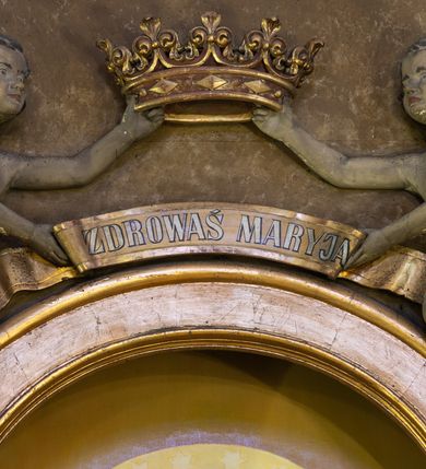 Zdjęcie nr 4: Jednokondygnacyjny, jednoosiowy ołtarz przyścienny ze zwieńczeniem uzyskał strukturę architektoniczną. Stipes ołtarzowy wykonano w formie wklęsło-wypukłego sarkofagu, zwężającego się ku dołowi, ujętego akantowymi wolutami. Na jego licu w centrum umieszczono płaskorzeźbiony medalion z monogramem maryjnym, ujęty symetryczną dekoracją roślinną, utworzoną z wici akantu oraz kwiatów. Retabulum zostało ustawione na wysokim, dwudzielnym cokole. Cokół zwieńczony profilowanym gzymsem udekorowano płycinami, które w wyższej kondygnacji wypełnione zostały dekoracją akantową. Nastawa po bokach ujęta została zdwojonymi kolumnami, umieszczonymi na prostopadłościennych postumentach z  symetryczną dekoracją utworzoną z akantu i kwiatów. Kapitele kolumn są kompozytowe, zaś trzony do jednej trzeciej wysokości zdobione zostały kanelurami. Kolumny podtrzymują odcinki pełnego belkowania, na których umieszczone są odcinki przerwanego przyczółka z umieszczonymi na nich figurami aniołów. Zwieńczenie ma formę zbliżoną do prostokąta zamkniętego od góry antytetycznie ustawionymi wolutami. Pomiędzy nimi na osi umieszczono na tle glorii promienistej złocony krzyż o trójlistnie zakończonych ramionach. W polu ołtarza usytuowano płycinę zamkniętą łukiem nadwieszonym z obrazem Matki Boskiej Szkaplerznej z Dzieciątkiem. Ponad obrazem znalazły się dwie rzeźbione figury aniołów podtrzymujących koronę oraz złoconą banderole z napisem: "ZDROWAŚ  MARIO". W zwieńczeniu umieszczono obraz św. Floriana w kształcie stojącego prostokąta o wklęsłych bokach, ściętych narożach i zamkniętego łukiem wklęsło-wypukłym. Struktura ołtarza została polichromowana w odcieniach brązu i czerni, natomiast ornamentykę i detale architektoniczne wyzłocono.