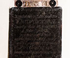 Zdjęcie nr 1: Płytowe epitafium ścienne składa się z trzech zasadniczych części - konsoli, płyty właściwej i zwieńczenia. Całość wspiera się na prostopadłościennej konsoli mającej formę leżącego, wydłużonego prostokąta. Na niej ustawiono czworoboczną płytę z inskrypcją wspartą na dwóch trapezoidalnych nóżkach, z dłuższym bokiem u góry. Płytę przy krawędziach ozdobiono ornamentem roślinnym tworzącym dekoracyjną bordiurę. Pole w całości wypełnia napis: "Magdalenie z Ostrzeszewiczów / WRONOWSKIEY / Zmarłey dnia 8[ósme]go Maia 1823 / w Roku życia 76 / przywiązane Dzieci / nayukochańszey Matce swoiey / Pomnik ten niewygasłego żalu kładą / Przechodzących / prosząc o westchnienie do Boga za Jey / Duszę". Na płycie wsparto na okrągłych podporach, pierwotnie zdobionych aplikacjami z brązu, zwieńczenie w formie płaskiego obelisku o ściętym wierzchołku. Jego pole zdobi profilowane obramienie oraz ryta arkatura. Na szczycie znajduje się półwypukła waza. Pomiędzy podporami obelisku umieszczono wykonane z brązu litery: "D[eo] O[pitmo] M[aximo]".