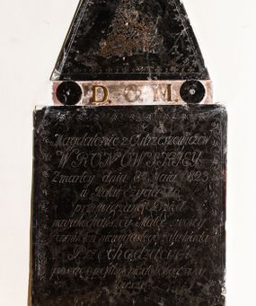 Zdjęcie nr 1: Płytowe epitafium ścienne składa się z trzech zasadniczych części - konsoli, płyty właściwej i zwieńczenia. Całość wspiera się na prostopadłościennej konsoli mającej formę leżącego, wydłużonego prostokąta. Na niej ustawiono czworoboczną płytę z inskrypcją wspartą na dwóch trapezoidalnych nóżkach, z dłuższym bokiem u góry. Płytę przy krawędziach ozdobiono ornamentem roślinnym tworzącym dekoracyjną bordiurę. Pole w całości wypełnia napis: "Magdalenie z Ostrzeszewiczów / WRONOWSKIEY / Zmarłey dnia 8[ósme]go Maia 1823 / w Roku życia 76 / przywiązane Dzieci / nayukochańszey Matce swoiey / Pomnik ten niewygasłego żalu kładą / Przechodzących / prosząc o westchnienie do Boga za Jey / Duszę". Na płycie wsparto na okrągłych podporach, pierwotnie zdobionych aplikacjami z brązu, zwieńczenie w formie płaskiego obelisku o ściętym wierzchołku. Jego pole zdobi profilowane obramienie oraz ryta arkatura. Na szczycie znajduje się półwypukła waza. Pomiędzy podporami obelisku umieszczono wykonane z brązu litery: "D[eo] O[pitmo] M[aximo]".