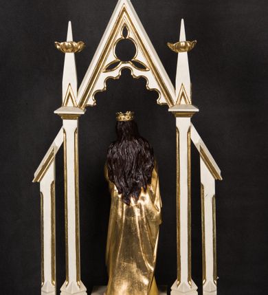 Zdjęcie nr 2: Na prostopadłościennej podstawie przeprutej otworami umożliwiającymi zakładzie drążków do noszenia ustawiono ażurowe obramienie ujmujące pełnoplastyczną rzeźbę św. Barbary. Bok podstawy zdobi złocony ornament liściasto-roślinny. Świętą ustawiono na czworobocznym postumencie. Jest to młoda kobieta ukazana frontalnie w kontrapoście. Lewą rękę przyciska do piersi, w prawej trzyma gałązkę palmową. Barbara ma pociągłą twarz o jasnej karnacji, prostym nosie i wąskich ustach. Jej głowę okalają długie włosy spływające na ramiona. Na głowie ma złoconą, otwartą koronę o prostych sterczynach. Ubrana jest w długą suknię i mocno drapowany płaszcz okrywający jej postać. Rozpięte ponad nią obramienie utworzono z wimpergi dekorowanej arkaturą i stylizowanym maswerkiem w części górnej, zwieńczoną pinaklem z kwiatonem. Wspiera się ona na dwóch wielobocznych filarach wspartych na cokolikach i przechodzących w dwa pinakle z kwiatonami. Oba filary po bokach wspierają przypory w formie podobnych, wielobocznych filarków na cokolikach u góry połączonych z resztą konstrukcji za pomocą daszków pulpitowych. Całość struktury feretronu polichromowano na biało, profile i kwiatony zostały pozłocone. 