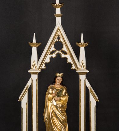 Zdjęcie nr 1: Na prostopadłościennej podstawie przeprutej otworami umożliwiającymi zakładzie drążków do noszenia ustawiono ażurowe obramienie ujmujące pełnoplastyczną rzeźbę św. Barbary. Bok podstawy zdobi złocony ornament liściasto-roślinny. Świętą ustawiono na czworobocznym postumencie. Jest to młoda kobieta ukazana frontalnie w kontrapoście. Lewą rękę przyciska do piersi, w prawej trzyma gałązkę palmową. Barbara ma pociągłą twarz o jasnej karnacji, prostym nosie i wąskich ustach. Jej głowę okalają długie włosy spływające na ramiona. Na głowie ma złoconą, otwartą koronę o prostych sterczynach. Ubrana jest w długą suknię i mocno drapowany płaszcz okrywający jej postać. Rozpięte ponad nią obramienie utworzono z wimpergi dekorowanej arkaturą i stylizowanym maswerkiem w części górnej, zwieńczoną pinaklem z kwiatonem. Wspiera się ona na dwóch wielobocznych filarach wspartych na cokolikach i przechodzących w dwa pinakle z kwiatonami. Oba filary po bokach wspierają przypory w formie podobnych, wielobocznych filarków na cokolikach u góry połączonych z resztą konstrukcji za pomocą daszków pulpitowych. Całość struktury feretronu polichromowano na biało, profile i kwiatony zostały pozłocone. 