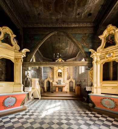 Zdjęcie nr 17: Kościół stanowi orientowaną, drewnianą świątynie wzniesioną na zrąb w układzie salowym z nawą na rzucie zbliżonym do kwadratu. Od wschody do nawy przylega węższe, prostokątne prezbiterium zamknięte trójbocznie. Od północy do prezbiterium dostawiono drewnianą zakrystię połączoną za pomocą portalu z prezbiterium kościoła. Do nawy od zachodu dostawiono czworoboczną wieżę o pochyłych ścianach, wzniesioną w konstrukcji słupowej. Wieńczy ją nadwieszona, czworoboczna izbica z ostrosłupowym, gontowym hełmem z krzyżem. W przyziemiach wieży urządzono kruchtę połączoną z nawą świątyni. Od północy, wschodu i południa kościół otaczają otwarte soboty, szalowane przy wieży. Elewacje zewnętrze zostały oszalowane lub też pokryte gontem. W nawie i prezbiterium przepruto okna parzyste, czworoboczne. Całość nakrywa dach gontowy o jednej kalenicy. Nad nawą w części wschodniej nadwieszono wieloboczną sygnaturkę w formie latarni z baniastym hełmem. Wnętrze nakryto stropami, dodatków w nawie z zaskrzynieniami. Pomiędzy prezbiterium, a nawą rozpięta jest ostrołukowa tęcza z fazowaną belką zawieszoną na kroksztynach z ustawionym na osi krucyfiksem. W zachodniej części nawy urządzono chór muzyczny o drewnianym, pełnym parapecie wklęsło-wypukłym z lambrekinem, wspartym na dwóch żłobkowanych kolumnach. Odrzwia południowe prowadzące do nawy ujęto w portal wycięty w ośli grzbiet. W prezbiterium ustawiono ołtarz główny, a w nawie dwa ołtarze boczne. 