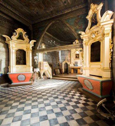 Zdjęcie nr 18: Kościół stanowi orientowaną, drewnianą świątynie wzniesioną na zrąb w układzie salowym z nawą na rzucie zbliżonym do kwadratu. Od wschody do nawy przylega węższe, prostokątne prezbiterium zamknięte trójbocznie. Od północy do prezbiterium dostawiono drewnianą zakrystię połączoną za pomocą portalu z prezbiterium kościoła. Do nawy od zachodu dostawiono czworoboczną wieżę o pochyłych ścianach, wzniesioną w konstrukcji słupowej. Wieńczy ją nadwieszona, czworoboczna izbica z ostrosłupowym, gontowym hełmem z krzyżem. W przyziemiach wieży urządzono kruchtę połączoną z nawą świątyni. Od północy, wschodu i południa kościół otaczają otwarte soboty, szalowane przy wieży. Elewacje zewnętrze zostały oszalowane lub też pokryte gontem. W nawie i prezbiterium przepruto okna parzyste, czworoboczne. Całość nakrywa dach gontowy o jednej kalenicy. Nad nawą w części wschodniej nadwieszono wieloboczną sygnaturkę w formie latarni z baniastym hełmem. Wnętrze nakryto stropami, dodatków w nawie z zaskrzynieniami. Pomiędzy prezbiterium, a nawą rozpięta jest ostrołukowa tęcza z fazowaną belką zawieszoną na kroksztynach z ustawionym na osi krucyfiksem. W zachodniej części nawy urządzono chór muzyczny o drewnianym, pełnym parapecie wklęsło-wypukłym z lambrekinem, wspartym na dwóch żłobkowanych kolumnach. Odrzwia południowe prowadzące do nawy ujęto w portal wycięty w ośli grzbiet. W prezbiterium ustawiono ołtarz główny, a w nawie dwa ołtarze boczne. 