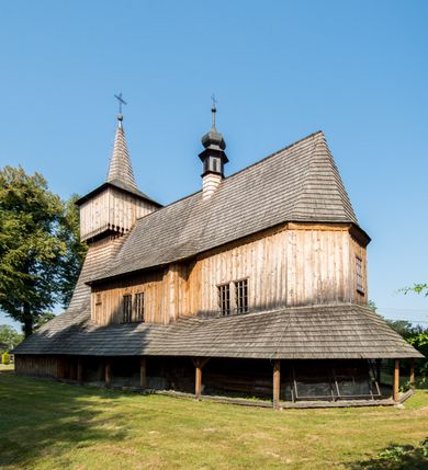 Zdjęcie nr 14: Kościół stanowi orientowaną, drewnianą świątynie wzniesioną na zrąb w układzie salowym z nawą na rzucie zbliżonym do kwadratu. Od wschody do nawy przylega węższe, prostokątne prezbiterium zamknięte trójbocznie. Od północy do prezbiterium dostawiono drewnianą zakrystię połączoną za pomocą portalu z prezbiterium kościoła. Do nawy od zachodu dostawiono czworoboczną wieżę o pochyłych ścianach, wzniesioną w konstrukcji słupowej. Wieńczy ją nadwieszona, czworoboczna izbica z ostrosłupowym, gontowym hełmem z krzyżem. W przyziemiach wieży urządzono kruchtę połączoną z nawą świątyni. Od północy, wschodu i południa kościół otaczają otwarte soboty, szalowane przy wieży. Elewacje zewnętrze zostały oszalowane lub też pokryte gontem. W nawie i prezbiterium przepruto okna parzyste, czworoboczne. Całość nakrywa dach gontowy o jednej kalenicy. Nad nawą w części wschodniej nadwieszono wieloboczną sygnaturkę w formie latarni z baniastym hełmem. Wnętrze nakryto stropami, dodatków w nawie z zaskrzynieniami. Pomiędzy prezbiterium, a nawą rozpięta jest ostrołukowa tęcza z fazowaną belką zawieszoną na kroksztynach z ustawionym na osi krucyfiksem. W zachodniej części nawy urządzono chór muzyczny o drewnianym, pełnym parapecie wklęsło-wypukłym z lambrekinem, wspartym na dwóch żłobkowanych kolumnach. Odrzwia południowe prowadzące do nawy ujęto w portal wycięty w ośli grzbiet. W prezbiterium ustawiono ołtarz główny, a w nawie dwa ołtarze boczne. 