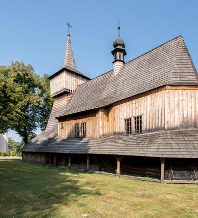 Zdjęcie nr 11: Kościół stanowi orientowaną, drewnianą świątynie wzniesioną na zrąb w układzie salowym z nawą na rzucie zbliżonym do kwadratu. Od wschody do nawy przylega węższe, prostokątne prezbiterium zamknięte trójbocznie. Od północy do prezbiterium dostawiono drewnianą zakrystię połączoną za pomocą portalu z prezbiterium kościoła. Do nawy od zachodu dostawiono czworoboczną wieżę o pochyłych ścianach, wzniesioną w konstrukcji słupowej. Wieńczy ją nadwieszona, czworoboczna izbica z ostrosłupowym, gontowym hełmem z krzyżem. W przyziemiach wieży urządzono kruchtę połączoną z nawą świątyni. Od północy, wschodu i południa kościół otaczają otwarte soboty, szalowane przy wieży. Elewacje zewnętrze zostały oszalowane lub też pokryte gontem. W nawie i prezbiterium przepruto okna parzyste, czworoboczne. Całość nakrywa dach gontowy o jednej kalenicy. Nad nawą w części wschodniej nadwieszono wieloboczną sygnaturkę w formie latarni z baniastym hełmem. Wnętrze nakryto stropami, dodatków w nawie z zaskrzynieniami. Pomiędzy prezbiterium, a nawą rozpięta jest ostrołukowa tęcza z fazowaną belką zawieszoną na kroksztynach z ustawionym na osi krucyfiksem. W zachodniej części nawy urządzono chór muzyczny o drewnianym, pełnym parapecie wklęsło-wypukłym z lambrekinem, wspartym na dwóch żłobkowanych kolumnach. Odrzwia południowe prowadzące do nawy ujęto w portal wycięty w ośli grzbiet. W prezbiterium ustawiono ołtarz główny, a w nawie dwa ołtarze boczne. 