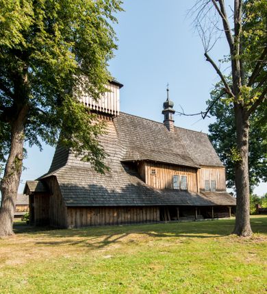 Zdjęcie nr 2: Kościół stanowi orientowaną, drewnianą świątynie wzniesioną na zrąb w układzie salowym z nawą na rzucie zbliżonym do kwadratu. Od wschody do nawy przylega węższe, prostokątne prezbiterium zamknięte trójbocznie. Od północy do prezbiterium dostawiono drewnianą zakrystię połączoną za pomocą portalu z prezbiterium kościoła. Do nawy od zachodu dostawiono czworoboczną wieżę o pochyłych ścianach, wzniesioną w konstrukcji słupowej. Wieńczy ją nadwieszona, czworoboczna izbica z ostrosłupowym, gontowym hełmem z krzyżem. W przyziemiach wieży urządzono kruchtę połączoną z nawą świątyni. Od północy, wschodu i południa kościół otaczają otwarte soboty, szalowane przy wieży. Elewacje zewnętrze zostały oszalowane lub też pokryte gontem. W nawie i prezbiterium przepruto okna parzyste, czworoboczne. Całość nakrywa dach gontowy o jednej kalenicy. Nad nawą w części wschodniej nadwieszono wieloboczną sygnaturkę w formie latarni z baniastym hełmem. Wnętrze nakryto stropami, dodatków w nawie z zaskrzynieniami. Pomiędzy prezbiterium, a nawą rozpięta jest ostrołukowa tęcza z fazowaną belką zawieszoną na kroksztynach z ustawionym na osi krucyfiksem. W zachodniej części nawy urządzono chór muzyczny o drewnianym, pełnym parapecie wklęsło-wypukłym z lambrekinem, wspartym na dwóch żłobkowanych kolumnach. Odrzwia południowe prowadzące do nawy ujęto w portal wycięty w ośli grzbiet. W prezbiterium ustawiono ołtarz główny, a w nawie dwa ołtarze boczne. 