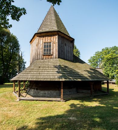 Zdjęcie nr 12: Kościół stanowi orientowaną, drewnianą świątynie wzniesioną na zrąb w układzie salowym z nawą na rzucie zbliżonym do kwadratu. Od wschody do nawy przylega węższe, prostokątne prezbiterium zamknięte trójbocznie. Od północy do prezbiterium dostawiono drewnianą zakrystię połączoną za pomocą portalu z prezbiterium kościoła. Do nawy od zachodu dostawiono czworoboczną wieżę o pochyłych ścianach, wzniesioną w konstrukcji słupowej. Wieńczy ją nadwieszona, czworoboczna izbica z ostrosłupowym, gontowym hełmem z krzyżem. W przyziemiach wieży urządzono kruchtę połączoną z nawą świątyni. Od północy, wschodu i południa kościół otaczają otwarte soboty, szalowane przy wieży. Elewacje zewnętrze zostały oszalowane lub też pokryte gontem. W nawie i prezbiterium przepruto okna parzyste, czworoboczne. Całość nakrywa dach gontowy o jednej kalenicy. Nad nawą w części wschodniej nadwieszono wieloboczną sygnaturkę w formie latarni z baniastym hełmem. Wnętrze nakryto stropami, dodatków w nawie z zaskrzynieniami. Pomiędzy prezbiterium, a nawą rozpięta jest ostrołukowa tęcza z fazowaną belką zawieszoną na kroksztynach z ustawionym na osi krucyfiksem. W zachodniej części nawy urządzono chór muzyczny o drewnianym, pełnym parapecie wklęsło-wypukłym z lambrekinem, wspartym na dwóch żłobkowanych kolumnach. Odrzwia południowe prowadzące do nawy ujęto w portal wycięty w ośli grzbiet. W prezbiterium ustawiono ołtarz główny, a w nawie dwa ołtarze boczne. 