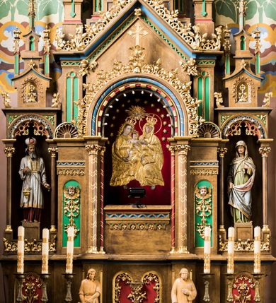 Zdjęcie nr 2: Trójosiowy ołtarz przyścienny uzyskał formę architektonicznej nastawy jednokondygnacyjnej ze zwieńczeniem. Sarkofagowy stipes ołtarzowy wsparto na profilowanym cokole, wieńcząc go gzymsem. Wspiera on drewnianą mensę z portatylem. Ołtarz ustawiono na podeście z dwoma gradusami. Retabulum zostało zaopatrzone w wysoki, drewniany cokół zwieńczony dekoracyjną listwą z motywami roślinno-kwiatowymi. Na cokole ustawiono trójosiową predellę. Jej środkową część wydzielono za pomocą wysokich, fazowanych postumentów, pomiędzy którymi znalazła się płycina z połączonymi ze sobą dwiema arkadami, których łuki przechodzą na profilowany wspornik ozdobiony ornamentem roślinno-kwiatowym. Płaskorzeźbiony ornament roślinno-kwiatowy poprowadzono także w świetle arkady. Po bokach widoczne są dwie kolejne, półkoliste arkady z podłuczami wypełnionymi arkaturą o czerwonych polach z płaskorzeźbionym ornamentem kwiatowo-roślinnym. W kondygnacji na osi środkowej usytuowano półkolistą arkadę ze zdwojonymi archiwoltami, wspartymi na podwójnych półkolumnach, o prostych bazach i kapitelach z motywem roślinnym. Arkadę flankują postumenty z półkoliście zamkniętymi płycinami o zielonych polach, wypełnionych płaskorzeźbionymi, skrzydlatymi główkami aniołków i motywami roślinnymi. Ponad gzymsem znalazły się półkoliste muszle. Arkadę zdobi biegnący po zewnętrznej ornament utworzony ze stylizowanych liści oraz szyszek, przedzielony na osi krzyżem. We wnętrz arkady umieszczono obraz w kształcie prostokąta zakończony półkoliście z przedstawieniem św. Anny Samotrzeć, dekorowany sukienką wotywną, nałożoną na aksamitne tło. Obraz zasłaniają dwie zasuwy z przedstawieniem Matki Boskiej Nieustającej Pomocy i św. Józefa. Poniżej obrazu widoczny jest parapet cokołu wprowadzonego w dolnej części arkady. Arkadę wieńczy belkowanie wyłamane na osi w formie nadwieszonego trójkąta, wsparte na dwóch  postumentach. Szczyt dekoruje ornament roślinny z motywem kół oraz ćwierci półkolistych muszli i stylizowany neogotycki kwiaton. Postumenty, wypełnione zaślepionym maswerkiem, ponad gzymsem przechodzą w dwie czworoboczne fiale, zakończone ostrosłupowym zwieńczeniem dekorowanym żabkami i kwiatonami, przechodzącymi w krzyże o trójlistnie zakończonych ramionach. W dolnych częściach fial usytuowano wycinane, trójlistne, zielone płyciny z motywem koniczyny przechodzące w listewki zakończone trójlistnie. Pomiędzy fialami wypiętrzono zwieńczenie utworzone z ostrołukowej arkady wspartej na zdwojonych półkolumnach. Na szczycie arkady umieszczono stylizowany neogotycki kwiaton, a po bokach płaskorzeźbione ornamenty kwiatowo-roślinne. Pod arkadą w polu zwieńczenia umieszczono prostokątny obraz zamknięty półkoliście z przedstawieniem Archanioła Rafała i Tobiasza. W osiach bocznych retabulum na poziomie kondygnacji znalazły się dwie wnęki arkadowe wsparte na kolumnach o roślinnych kapitelach i prostych bazach, umieszczonych na niskich cokołach. Całość została wsparta na cokoliku dekorowanym ornamentem roślinnym. Półkoliste arkady wypełniono pseudogotyckim maswerkiem. We wnękach ustawiono pełnoplastyczne rzeźby św. Zachariasza i św. Elżbiety. Powyżej usytuowano dekoracyjne zwieńczenie nawiązujące do pseudogotyckich fial z trzema sterczynami.