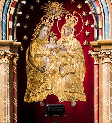 Zdjęcie nr 5: Trójosiowy ołtarz przyścienny uzyskał formę architektonicznej nastawy jednokondygnacyjnej ze zwieńczeniem. Sarkofagowy stipes ołtarzowy wsparto na profilowanym cokole, wieńcząc go gzymsem. Wspiera on drewnianą mensę z portatylem. Ołtarz ustawiono na podeście z dwoma gradusami. Retabulum zostało zaopatrzone w wysoki, drewniany cokół zwieńczony dekoracyjną listwą z motywami roślinno-kwiatowymi. Na cokole ustawiono trójosiową predellę. Jej środkową część wydzielono za pomocą wysokich, fazowanych postumentów, pomiędzy którymi znalazła się płycina z połączonymi ze sobą dwiema arkadami, których łuki przechodzą na profilowany wspornik ozdobiony ornamentem roślinno-kwiatowym. Płaskorzeźbiony ornament roślinno-kwiatowy poprowadzono także w świetle arkady. Po bokach widoczne są dwie kolejne, półkoliste arkady z podłuczami wypełnionymi arkaturą o czerwonych polach z płaskorzeźbionym ornamentem kwiatowo-roślinnym. W kondygnacji na osi środkowej usytuowano półkolistą arkadę ze zdwojonymi archiwoltami, wspartymi na podwójnych półkolumnach, o prostych bazach i kapitelach z motywem roślinnym. Arkadę flankują postumenty z półkoliście zamkniętymi płycinami o zielonych polach, wypełnionych płaskorzeźbionymi, skrzydlatymi główkami aniołków i motywami roślinnymi. Ponad gzymsem znalazły się półkoliste muszle. Arkadę zdobi biegnący po zewnętrznej ornament utworzony ze stylizowanych liści oraz szyszek, przedzielony na osi krzyżem. We wnętrz arkady umieszczono obraz w kształcie prostokąta zakończony półkoliście z przedstawieniem św. Anny Samotrzeć, dekorowany sukienką wotywną, nałożoną na aksamitne tło. Obraz zasłaniają dwie zasuwy z przedstawieniem Matki Boskiej Nieustającej Pomocy i św. Józefa. Poniżej obrazu widoczny jest parapet cokołu wprowadzonego w dolnej części arkady. Arkadę wieńczy belkowanie wyłamane na osi w formie nadwieszonego trójkąta, wsparte na dwóch  postumentach. Szczyt dekoruje ornament roślinny z motywem kół oraz ćwierci półkolistych muszli i stylizowany neogotycki kwiaton. Postumenty, wypełnione zaślepionym maswerkiem, ponad gzymsem przechodzą w dwie czworoboczne fiale, zakończone ostrosłupowym zwieńczeniem dekorowanym żabkami i kwiatonami, przechodzącymi w krzyże o trójlistnie zakończonych ramionach. W dolnych częściach fial usytuowano wycinane, trójlistne, zielone płyciny z motywem koniczyny przechodzące w listewki zakończone trójlistnie. Pomiędzy fialami wypiętrzono zwieńczenie utworzone z ostrołukowej arkady wspartej na zdwojonych półkolumnach. Na szczycie arkady umieszczono stylizowany neogotycki kwiaton, a po bokach płaskorzeźbione ornamenty kwiatowo-roślinne. Pod arkadą w polu zwieńczenia umieszczono prostokątny obraz zamknięty półkoliście z przedstawieniem Archanioła Rafała i Tobiasza. W osiach bocznych retabulum na poziomie kondygnacji znalazły się dwie wnęki arkadowe wsparte na kolumnach o roślinnych kapitelach i prostych bazach, umieszczonych na niskich cokołach. Całość została wsparta na cokoliku dekorowanym ornamentem roślinnym. Półkoliste arkady wypełniono pseudogotyckim maswerkiem. We wnękach ustawiono pełnoplastyczne rzeźby św. Zachariasza i św. Elżbiety. Powyżej usytuowano dekoracyjne zwieńczenie nawiązujące do pseudogotyckich fial z trzema sterczynami.