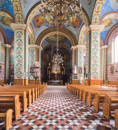 Zdjęcie nr 12: Orientowany kościół pw. Wszystkich Świętych w Wieprzu został wzniesiony w układzie trójnawowej hali z prostokątnym prezbiterium zamkniętym płaską apsydą na przedłużeniu nawy głównej, flankowanego od południa kaplicą, a od północy piętrową zakrystią. Od zachodu do trójprzęsłowego korpusu nawowego dostawiono nieznacznie wysuniętą do przodu czworoboczną wieżę, flankowaną po bokach dwoma aneksami tej samej wysokości, co nawa i aneksy przy prezbiterium. Całość nakryto miedzianym dachem siodłowym. Przy końcu nawy od wschodu na dachu nadwieszono sygnaturkę w formie latarni zwieńczonej ostrosłupowym hełmem. Elewacje zewnętrzne przeprute półokrągłymi oknami artykułowano za pomocą pilastrów o prostych głowicach wspartych na wysoki cokołach połączonych ze sobą gzymsem, podtrzymujących fazowane belkowanie przechodzące w profilowany gzyms koronujący. Elewacje wieży podzielona na dwie strefy rozdzielone belkowaniem wyłamanym w partii masywu wieżowego. W dolnej strefie w przyziemiu urządzono kruchtę, do której wejście na osi flankowane jest masywnym portalem utworzonym z dwóch czworobocznych podpór wspierających trójkątny przyczółek, ponad którym przepruto półokrągłe okno. Ponad gzymsem, w górnej strefie, zastosowano podział ramowy, ujmujący okulus, który pełni partię cokołową wspierającą flankujące górną część wieży pary pilastrów na każdej z czterech elewacji. Pilastry ustawione na postumentach o gładkich trzonach i kompozytowych głowicach wspierają fazowane belkowanie przechodzące w gzyms koronujący. Pomiędzy pilastrami przepruto półokrągłe okna z umieszczonymi nad nimi trójkątnymi przyczółkami. Gzyms został wyłamany na każdej z osi środkowej, tworząc miejsce dla tarcz zegarowych. Wieżę zwieńczono baniastym hełmem z czworoboczną latarnią nakrytą cebulastym zwieńczeniem z krzyżem. Nawa główna otwiera się do naw bocznych z każdej strony otwiera się do naw bocznych z każdej strony trzema opilastrowanymi arkadami filarowymi. Wnętrze nakryto sklepieniem krzyżowym. Chór muzyczny zajmuje szerokość całego korpusu nawowego, wspierając się na pięciu arkadach - trzy w nawie głównej i po jednej w nawach bocznych. Balustrada na chórze artykułowana jest płycinami rozdzielonymi niskim postumentami. W prezbiterium ustawiono ołtarz główny, a na zakończeniu naw ołtarze boczne. Dwa ołtarze boczne znalazły się także w części zachodniej nawy południowej i północnej.