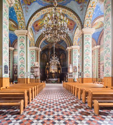 Zdjęcie nr 11: Orientowany kościół pw. Wszystkich Świętych w Wieprzu został wzniesiony w układzie trójnawowej hali z prostokątnym prezbiterium zamkniętym płaską apsydą na przedłużeniu nawy głównej, flankowanego od południa kaplicą, a od północy piętrową zakrystią. Od zachodu do trójprzęsłowego korpusu nawowego dostawiono nieznacznie wysuniętą do przodu czworoboczną wieżę, flankowaną po bokach dwoma aneksami tej samej wysokości, co nawa i aneksy przy prezbiterium. Całość nakryto miedzianym dachem siodłowym. Przy końcu nawy od wschodu na dachu nadwieszono sygnaturkę w formie latarni zwieńczonej ostrosłupowym hełmem. Elewacje zewnętrzne przeprute półokrągłymi oknami artykułowano za pomocą pilastrów o prostych głowicach wspartych na wysoki cokołach połączonych ze sobą gzymsem, podtrzymujących fazowane belkowanie przechodzące w profilowany gzyms koronujący. Elewacje wieży podzielona na dwie strefy rozdzielone belkowaniem wyłamanym w partii masywu wieżowego. W dolnej strefie w przyziemiu urządzono kruchtę, do której wejście na osi flankowane jest masywnym portalem utworzonym z dwóch czworobocznych podpór wspierających trójkątny przyczółek, ponad którym przepruto półokrągłe okno. Ponad gzymsem, w górnej strefie, zastosowano podział ramowy, ujmujący okulus, który pełni partię cokołową wspierającą flankujące górną część wieży pary pilastrów na każdej z czterech elewacji. Pilastry ustawione na postumentach o gładkich trzonach i kompozytowych głowicach wspierają fazowane belkowanie przechodzące w gzyms koronujący. Pomiędzy pilastrami przepruto półokrągłe okna z umieszczonymi nad nimi trójkątnymi przyczółkami. Gzyms został wyłamany na każdej z osi środkowej, tworząc miejsce dla tarcz zegarowych. Wieżę zwieńczono baniastym hełmem z czworoboczną latarnią nakrytą cebulastym zwieńczeniem z krzyżem. Nawa główna otwiera się do naw bocznych z każdej strony otwiera się do naw bocznych z każdej strony trzema opilastrowanymi arkadami filarowymi. Wnętrze nakryto sklepieniem krzyżowym. Chór muzyczny zajmuje szerokość całego korpusu nawowego, wspierając się na pięciu arkadach - trzy w nawie głównej i po jednej w nawach bocznych. Balustrada na chórze artykułowana jest płycinami rozdzielonymi niskim postumentami. W prezbiterium ustawiono ołtarz główny, a na zakończeniu naw ołtarze boczne. Dwa ołtarze boczne znalazły się także w części zachodniej nawy południowej i północnej.