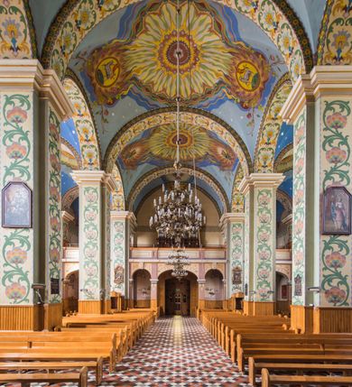 Zdjęcie nr 23: Orientowany kościół pw. Wszystkich Świętych w Wieprzu został wzniesiony w układzie trójnawowej hali z prostokątnym prezbiterium zamkniętym płaską apsydą na przedłużeniu nawy głównej, flankowanego od południa kaplicą, a od północy piętrową zakrystią. Od zachodu do trójprzęsłowego korpusu nawowego dostawiono nieznacznie wysuniętą do przodu czworoboczną wieżę, flankowaną po bokach dwoma aneksami tej samej wysokości, co nawa i aneksy przy prezbiterium. Całość nakryto miedzianym dachem siodłowym. Przy końcu nawy od wschodu na dachu nadwieszono sygnaturkę w formie latarni zwieńczonej ostrosłupowym hełmem. Elewacje zewnętrzne przeprute półokrągłymi oknami artykułowano za pomocą pilastrów o prostych głowicach wspartych na wysoki cokołach połączonych ze sobą gzymsem, podtrzymujących fazowane belkowanie przechodzące w profilowany gzyms koronujący. Elewacje wieży podzielona na dwie strefy rozdzielone belkowaniem wyłamanym w partii masywu wieżowego. W dolnej strefie w przyziemiu urządzono kruchtę, do której wejście na osi flankowane jest masywnym portalem utworzonym z dwóch czworobocznych podpór wspierających trójkątny przyczółek, ponad którym przepruto półokrągłe okno. Ponad gzymsem, w górnej strefie, zastosowano podział ramowy, ujmujący okulus, który pełni partię cokołową wspierającą flankujące górną część wieży pary pilastrów na każdej z czterech elewacji. Pilastry ustawione na postumentach o gładkich trzonach i kompozytowych głowicach wspierają fazowane belkowanie przechodzące w gzyms koronujący. Pomiędzy pilastrami przepruto półokrągłe okna z umieszczonymi nad nimi trójkątnymi przyczółkami. Gzyms został wyłamany na każdej z osi środkowej, tworząc miejsce dla tarcz zegarowych. Wieżę zwieńczono baniastym hełmem z czworoboczną latarnią nakrytą cebulastym zwieńczeniem z krzyżem. Nawa główna otwiera się do naw bocznych z każdej strony otwiera się do naw bocznych z każdej strony trzema opilastrowanymi arkadami filarowymi. Wnętrze nakryto sklepieniem krzyżowym. Chór muzyczny zajmuje szerokość całego korpusu nawowego, wspierając się na pięciu arkadach - trzy w nawie głównej i po jednej w nawach bocznych. Balustrada na chórze artykułowana jest płycinami rozdzielonymi niskim postumentami. W prezbiterium ustawiono ołtarz główny, a na zakończeniu naw ołtarze boczne. Dwa ołtarze boczne znalazły się także w części zachodniej nawy południowej i północnej.