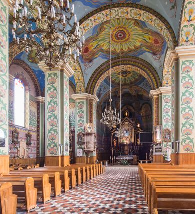 Zdjęcie nr 14: Orientowany kościół pw. Wszystkich Świętych w Wieprzu został wzniesiony w układzie trójnawowej hali z prostokątnym prezbiterium zamkniętym płaską apsydą na przedłużeniu nawy głównej, flankowanego od południa kaplicą, a od północy piętrową zakrystią. Od zachodu do trójprzęsłowego korpusu nawowego dostawiono nieznacznie wysuniętą do przodu czworoboczną wieżę, flankowaną po bokach dwoma aneksami tej samej wysokości, co nawa i aneksy przy prezbiterium. Całość nakryto miedzianym dachem siodłowym. Przy końcu nawy od wschodu na dachu nadwieszono sygnaturkę w formie latarni zwieńczonej ostrosłupowym hełmem. Elewacje zewnętrzne przeprute półokrągłymi oknami artykułowano za pomocą pilastrów o prostych głowicach wspartych na wysoki cokołach połączonych ze sobą gzymsem, podtrzymujących fazowane belkowanie przechodzące w profilowany gzyms koronujący. Elewacje wieży podzielona na dwie strefy rozdzielone belkowaniem wyłamanym w partii masywu wieżowego. W dolnej strefie w przyziemiu urządzono kruchtę, do której wejście na osi flankowane jest masywnym portalem utworzonym z dwóch czworobocznych podpór wspierających trójkątny przyczółek, ponad którym przepruto półokrągłe okno. Ponad gzymsem, w górnej strefie, zastosowano podział ramowy, ujmujący okulus, który pełni partię cokołową wspierającą flankujące górną część wieży pary pilastrów na każdej z czterech elewacji. Pilastry ustawione na postumentach o gładkich trzonach i kompozytowych głowicach wspierają fazowane belkowanie przechodzące w gzyms koronujący. Pomiędzy pilastrami przepruto półokrągłe okna z umieszczonymi nad nimi trójkątnymi przyczółkami. Gzyms został wyłamany na każdej z osi środkowej, tworząc miejsce dla tarcz zegarowych. Wieżę zwieńczono baniastym hełmem z czworoboczną latarnią nakrytą cebulastym zwieńczeniem z krzyżem. Nawa główna otwiera się do naw bocznych z każdej strony otwiera się do naw bocznych z każdej strony trzema opilastrowanymi arkadami filarowymi. Wnętrze nakryto sklepieniem krzyżowym. Chór muzyczny zajmuje szerokość całego korpusu nawowego, wspierając się na pięciu arkadach - trzy w nawie głównej i po jednej w nawach bocznych. Balustrada na chórze artykułowana jest płycinami rozdzielonymi niskim postumentami. W prezbiterium ustawiono ołtarz główny, a na zakończeniu naw ołtarze boczne. Dwa ołtarze boczne znalazły się także w części zachodniej nawy południowej i północnej.