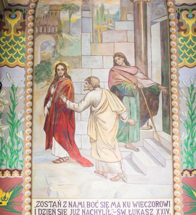 Zdjęcie nr 5: Dekoracja malarska wnętrza kościoła została oparta zasadniczo na motywach ornamentalnych, gdzie wyjątek stanowi monumentalna scena ukazująca uczniów idących do Emaus, usytuowana na północnej ścianie prezbiterium, nad wejściem do zakrystii. Wyobrażono tu w malowanym, ornamentalnym obramieniu scenę wpisaną w stojący prostokąt, zamknięty od góry łukiem półkolistym. W centrum kompozycji ukazano Chrystusa, którego zatrzymują stojący na schodach gospody dwaj uczniowie idący do Emaus. Stojący Zbawiciel został wyobrażony z lewej strony w trzech czwartych w prawo. Prawą ręką podtrzymuje połę płaszcza, lewa jest niewidoczna. Jest to dojrzały mężczyzna o pociągłej twarzy z wydatnym nosem i ustami, długimi włosami spływającymi na ramiona oraz brodą okalającą twarz o jasnej karnacji. Zbawiciel ubrany jest w białą tunikę i szkarłatny płaszcz. Do niego zwraca się jedne z uczniów ukazany tyłem do widza w trzech czwartych w lewo. Jest to dojrzały mężczyzna, który lewą rękę wyciąga w stronę Jezusa, prawą zaś zdaje się zapraszać do wejścia na schody. Jego twarz okolona krótkimi włosami z brodą i wydatnym nosem i ustami widoczna jest z profilu. Ubrany jest w jasną tunikę oraz jasnobeżowy płaszcz. Przed nim z prawej strony na stopniach wiodących do drzwi gospody stoi drugi uczeń. Ujęto go frontalnie w kontrapoście z głową w trzech czwartych w lewo. W prawej ręce trzyma laskę, lewą zaś wskazuje na drzwi zajazdu. Jest to młody mężczyzna o pociągłej twarzy i długich włosach spływających na plecy. Ubrany jest w przewiązaną w pasie tunikę oraz narzucony na ramiona bladoszkarłatny płaszcz. Za przedstawionymi postaciami widać fragment wschodniej architektury oraz rozbudowaną sekwencję pejzażową z elementem bramy miejskiej oraz roślinnością na tle wieczornego nieba. Poniżej przedstawienia umieszczono napis: &quot;Uczniowie z Emaus&quot; podpis: &quot;ZOSTAŃ Z NAMI, BOĆ SIĘ MA KU WIECZOROWI I DZIEŃ SIĘ JUŻ NACHYLIŁ - ŚW[IĘTY] ŁUKASZ XXIV&quot;. Bogactwo ornamentalnej dekoracji malarskiej zostało podporządkowane architekturze wnętrza. Partię ścian pokryto malaturą o charakterze dywanowym, ułożoną strefowo z powtarzających się rytmicznie kolorowych motywów ornamentalnych. Gurty sklepienne oraz trzony pilastrów na filarach międzynawowych pokryto wykonanymi na niebieskim lub błękitnym tle ornamentalnymi pasami z motywem fantazyjnych kwiatów i wici roślinnych. Partię sklepienne w kolejnych przęsłach w nawach udekorowano koncentrycznie rozchodzą się płomienistą i falującą ornamentyką, z wplecionymi motywami symbolu Najświętszego Serca Pana Jezusa, Apokaliptycznego Baranka, kielicha z hostią w otoczeniu kłosów zbóż i winnej latorośli, a także gałązek różanych i cierniowych. Na ścianach prezbiterium zastosowano podział strefowy. Dolne przestrzenie ozdobiono pasma ornamentalnymi. Powyżej rozmieszczono strefę z przedstawieniem rosnących obok siebie kwitów lilii. U samej góry sięgnięto do motywów rybich łusek oraz stylizowanej, wielobarwnej ornamentyki fantazyjnej. Gurty sklepienia udekorowano pasami opartymi na stylizowanych skrzydłach serafinów. Natomiast w poszczególnych polach sklepiennych na niebieskim tle w fantazyjnych, falujących otokach wyobrażono dwa skrzyżowane płonące miecze, oko Opatrzności Bożej, dwie tablice Dekalogu. Na środkowej gurcie u szczytu w barwnym obramienium ukazano napis: &quot;KTÓŻ JAK BÓG&quot;. 