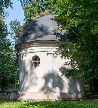 Zdjęcie nr 4: Kaplicę wzniesiono na rzucie koła, nakrywając jej wnętrze półkolistą kopułą. Ściany zewnętrzne zostały podzielone ośmioma pilastrami jońskimi, wspierającymi belkowanie. Powyżej belkowania biegnie profilowany gzyms koronujący, dekorowany fryzem kostkowym. Półokrągłe wejście usytuowano od zachodu. Prowadzi do niego pięć stopni. Wejście zamyka żelazna, klasycystyczna krata. Od wschodu w ścianie przepruto okulus, ujęty od wnętrza półokrągłym glifem w płytkiej, prostokątnej niszy zamkniętej półokrągło. Wnętrze pokryto ochrową polichromią, z wymalowanym białą kreską podziałem odzwierciedlającym artykulację zewnętrzną. Na ścianie umieszczono dwie czworoboczne płyty upamiętniające zmarłych pochowanych w krypcie. Wejście do krypty zamyka prostokątna, marmurowa płyta dekorowana aplikacją ze złoconego brązu, ukazującą trupią czaszkę ze skrzyżowanymi piszczelami umieszczoną nad antabą.