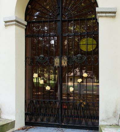 Zdjęcie nr 18: Kaplicę wzniesiono na rzucie koła, nakrywając jej wnętrze półkolistą kopułą. Ściany zewnętrzne zostały podzielone ośmioma pilastrami jońskimi, wspierającymi belkowanie. Powyżej belkowania biegnie profilowany gzyms koronujący, dekorowany fryzem kostkowym. Półokrągłe wejście usytuowano od zachodu. Prowadzi do niego pięć stopni. Wejście zamyka żelazna, klasycystyczna krata. Od wschodu w ścianie przepruto okulus, ujęty od wnętrza półokrągłym glifem w płytkiej, prostokątnej niszy zamkniętej półokrągło. Wnętrze pokryto ochrową polichromią, z wymalowanym białą kreską podziałem odzwierciedlającym artykulację zewnętrzną. Na ścianie umieszczono dwie czworoboczne płyty upamiętniające zmarłych pochowanych w krypcie. Wejście do krypty zamyka prostokątna, marmurowa płyta dekorowana aplikacją ze złoconego brązu, ukazującą trupią czaszkę ze skrzyżowanymi piszczelami umieszczoną nad antabą.