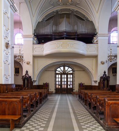 Zdjęcie nr 36: Kościół Wniebowzięcia Najświętszej Marii Panny w Oświęcimu jest świątynia murowaną, orientowaną. Dwuprzęsłowe prezbiterium zamknięte ścianą prostą wzniesiono na rzucie prostokąta. W jego narożach widoczne są przypory. Od południa wybudowano przy nim zakrystię, a od północy kaplicę Chrystusa Ukrzyżowanego, którą gruntownie przebudowano w stylu pseudoromańskim w latach dwudziestych XX wieku. Korpus kościoła uzyskał układ trójnawowej, dwuprzęsłowej hali. Od zachodu na osi wzniesiono czworoboczną, dwupoziomową wieżę. Pierwszy poziom, w którym urządzono kruchtę, jest zaopatrzony w narożach w uskokowe przypory. Natomiast drugi, wyraźnie zmniejszony, został wzniesiony ponad profilowanym gzymsem na rzucie czworobocznym o ściętych narożach. Całość nakryto ostrosłupowym hełmem zwieńczonym krzyżem, wspartym na trójkątnych przyczółkach stanowiących zakończenie ścian drugiego poziomu. Nawa główna otwiera się do naw bocznych z każdej strony poprzez dwiema opilastrowanymi arkadami filarowymi. Tęcza pomiędzy nawą, a prezbiterium uzyskała wykrój półkolisty. Wnetrze obu części kościoła nakryto sklepieniem kolebkowym z lunetami wsparte na gurtach. W części zachodniej kościoła na długości całego korpusu urządzono chór muzyczny wsparty na trzech arkadach z parapetem wygiętym łukowo pośrodku. Sklepienie i parapet chóru zostały udekorowane figurami geometrycznymi ze stiukowych listw profilowanych. Do południowej nawy bocznej prowadzi gotycki, ostrołukowy portal kamienny. Z kolei wejście do prezbiterium z zakrystii oraz z kruchty do północnej nawy bocznej obramieniają dwa prostokątne, kamienne portale gotycko-renesansowe. W prezbiterium ustawiono ołtarz główny, a dwa ołtarze boczne na wschodniej ścianie naw bocznych. Kolejny ołtarz boczny znalazł się po prawej stronie łuku tęczowego. Po jego zaś drugiej stronie zawieszono ambonę. 