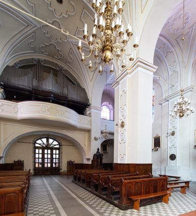 Zdjęcie nr 34: Kościół Wniebowzięcia Najświętszej Marii Panny w Oświęcimu jest świątynia murowaną, orientowaną. Dwuprzęsłowe prezbiterium zamknięte ścianą prostą wzniesiono na rzucie prostokąta. W jego narożach widoczne są przypory. Od południa wybudowano przy nim zakrystię, a od północy kaplicę Chrystusa Ukrzyżowanego, którą gruntownie przebudowano w stylu pseudoromańskim w latach dwudziestych XX wieku. Korpus kościoła uzyskał układ trójnawowej, dwuprzęsłowej hali. Od zachodu na osi wzniesiono czworoboczną, dwupoziomową wieżę. Pierwszy poziom, w którym urządzono kruchtę, jest zaopatrzony w narożach w uskokowe przypory. Natomiast drugi, wyraźnie zmniejszony, został wzniesiony ponad profilowanym gzymsem na rzucie czworobocznym o ściętych narożach. Całość nakryto ostrosłupowym hełmem zwieńczonym krzyżem, wspartym na trójkątnych przyczółkach stanowiących zakończenie ścian drugiego poziomu. Nawa główna otwiera się do naw bocznych z każdej strony poprzez dwiema opilastrowanymi arkadami filarowymi. Tęcza pomiędzy nawą, a prezbiterium uzyskała wykrój półkolisty. Wnetrze obu części kościoła nakryto sklepieniem kolebkowym z lunetami wsparte na gurtach. W części zachodniej kościoła na długości całego korpusu urządzono chór muzyczny wsparty na trzech arkadach z parapetem wygiętym łukowo pośrodku. Sklepienie i parapet chóru zostały udekorowane figurami geometrycznymi ze stiukowych listw profilowanych. Do południowej nawy bocznej prowadzi gotycki, ostrołukowy portal kamienny. Z kolei wejście do prezbiterium z zakrystii oraz z kruchty do północnej nawy bocznej obramieniają dwa prostokątne, kamienne portale gotycko-renesansowe. W prezbiterium ustawiono ołtarz główny, a dwa ołtarze boczne na wschodniej ścianie naw bocznych. Kolejny ołtarz boczny znalazł się po prawej stronie łuku tęczowego. Po jego zaś drugiej stronie zawieszono ambonę. 