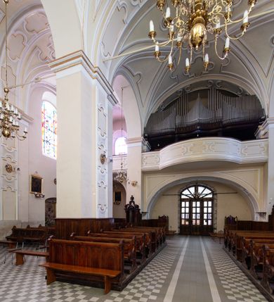 Zdjęcie nr 33: Kościół Wniebowzięcia Najświętszej Marii Panny w Oświęcimu jest świątynia murowaną, orientowaną. Dwuprzęsłowe prezbiterium zamknięte ścianą prostą wzniesiono na rzucie prostokąta. W jego narożach widoczne są przypory. Od południa wybudowano przy nim zakrystię, a od północy kaplicę Chrystusa Ukrzyżowanego, którą gruntownie przebudowano w stylu pseudoromańskim w latach dwudziestych XX wieku. Korpus kościoła uzyskał układ trójnawowej, dwuprzęsłowej hali. Od zachodu na osi wzniesiono czworoboczną, dwupoziomową wieżę. Pierwszy poziom, w którym urządzono kruchtę, jest zaopatrzony w narożach w uskokowe przypory. Natomiast drugi, wyraźnie zmniejszony, został wzniesiony ponad profilowanym gzymsem na rzucie czworobocznym o ściętych narożach. Całość nakryto ostrosłupowym hełmem zwieńczonym krzyżem, wspartym na trójkątnych przyczółkach stanowiących zakończenie ścian drugiego poziomu. Nawa główna otwiera się do naw bocznych z każdej strony poprzez dwiema opilastrowanymi arkadami filarowymi. Tęcza pomiędzy nawą, a prezbiterium uzyskała wykrój półkolisty. Wnetrze obu części kościoła nakryto sklepieniem kolebkowym z lunetami wsparte na gurtach. W części zachodniej kościoła na długości całego korpusu urządzono chór muzyczny wsparty na trzech arkadach z parapetem wygiętym łukowo pośrodku. Sklepienie i parapet chóru zostały udekorowane figurami geometrycznymi ze stiukowych listw profilowanych. Do południowej nawy bocznej prowadzi gotycki, ostrołukowy portal kamienny. Z kolei wejście do prezbiterium z zakrystii oraz z kruchty do północnej nawy bocznej obramieniają dwa prostokątne, kamienne portale gotycko-renesansowe. W prezbiterium ustawiono ołtarz główny, a dwa ołtarze boczne na wschodniej ścianie naw bocznych. Kolejny ołtarz boczny znalazł się po prawej stronie łuku tęczowego. Po jego zaś drugiej stronie zawieszono ambonę. 