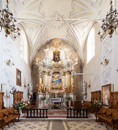 Zdjęcie nr 28: Kościół Wniebowzięcia Najświętszej Marii Panny w Oświęcimu jest świątynia murowaną, orientowaną. Dwuprzęsłowe prezbiterium zamknięte ścianą prostą wzniesiono na rzucie prostokąta. W jego narożach widoczne są przypory. Od południa wybudowano przy nim zakrystię, a od północy kaplicę Chrystusa Ukrzyżowanego, którą gruntownie przebudowano w stylu pseudoromańskim w latach dwudziestych XX wieku. Korpus kościoła uzyskał układ trójnawowej, dwuprzęsłowej hali. Od zachodu na osi wzniesiono czworoboczną, dwupoziomową wieżę. Pierwszy poziom, w którym urządzono kruchtę, jest zaopatrzony w narożach w uskokowe przypory. Natomiast drugi, wyraźnie zmniejszony, został wzniesiony ponad profilowanym gzymsem na rzucie czworobocznym o ściętych narożach. Całość nakryto ostrosłupowym hełmem zwieńczonym krzyżem, wspartym na trójkątnych przyczółkach stanowiących zakończenie ścian drugiego poziomu. Nawa główna otwiera się do naw bocznych z każdej strony poprzez dwiema opilastrowanymi arkadami filarowymi. Tęcza pomiędzy nawą, a prezbiterium uzyskała wykrój półkolisty. Wnetrze obu części kościoła nakryto sklepieniem kolebkowym z lunetami wsparte na gurtach. W części zachodniej kościoła na długości całego korpusu urządzono chór muzyczny wsparty na trzech arkadach z parapetem wygiętym łukowo pośrodku. Sklepienie i parapet chóru zostały udekorowane figurami geometrycznymi ze stiukowych listw profilowanych. Do południowej nawy bocznej prowadzi gotycki, ostrołukowy portal kamienny. Z kolei wejście do prezbiterium z zakrystii oraz z kruchty do północnej nawy bocznej obramieniają dwa prostokątne, kamienne portale gotycko-renesansowe. W prezbiterium ustawiono ołtarz główny, a dwa ołtarze boczne na wschodniej ścianie naw bocznych. Kolejny ołtarz boczny znalazł się po prawej stronie łuku tęczowego. Po jego zaś drugiej stronie zawieszono ambonę. 