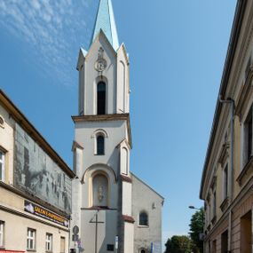 Zdjęcie nr 1: Kościół Wniebowzięcia Najświętszej Marii Panny w Oświęcimu jest świątynia murowaną, orientowaną. Dwuprzęsłowe prezbiterium zamknięte ścianą prostą wzniesiono na rzucie prostokąta. W jego narożach widoczne są przypory. Od południa wybudowano przy nim zakrystię, a od północy kaplicę Chrystusa Ukrzyżowanego, którą gruntownie przebudowano w stylu pseudoromańskim w latach dwudziestych XX wieku. Korpus kościoła uzyskał układ trójnawowej, dwuprzęsłowej hali. Od zachodu na osi wzniesiono czworoboczną, dwupoziomową wieżę. Pierwszy poziom, w którym urządzono kruchtę, jest zaopatrzony w narożach w uskokowe przypory. Natomiast drugi, wyraźnie zmniejszony, został wzniesiony ponad profilowanym gzymsem na rzucie czworobocznym o ściętych narożach. Całość nakryto ostrosłupowym hełmem zwieńczonym krzyżem, wspartym na trójkątnych przyczółkach stanowiących zakończenie ścian drugiego poziomu. Nawa główna otwiera się do naw bocznych z każdej strony poprzez dwiema opilastrowanymi arkadami filarowymi. Tęcza pomiędzy nawą, a prezbiterium uzyskała wykrój półkolisty. Wnetrze obu części kościoła nakryto sklepieniem kolebkowym z lunetami wsparte na gurtach. W części zachodniej kościoła na długości całego korpusu urządzono chór muzyczny wsparty na trzech arkadach z parapetem wygiętym łukowo pośrodku. Sklepienie i parapet chóru zostały udekorowane figurami geometrycznymi ze stiukowych listw profilowanych. Do południowej nawy bocznej prowadzi gotycki, ostrołukowy portal kamienny. Z kolei wejście do prezbiterium z zakrystii oraz z kruchty do północnej nawy bocznej obramieniają dwa prostokątne, kamienne portale gotycko-renesansowe. W prezbiterium ustawiono ołtarz główny, a dwa ołtarze boczne na wschodniej ścianie naw bocznych. Kolejny ołtarz boczny znalazł się po prawej stronie łuku tęczowego. Po jego zaś drugiej stronie zawieszono ambonę. 