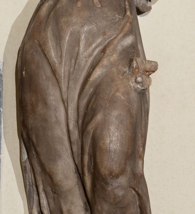 Zdjęcie nr 3: Przyścienna rzeźba ukazująca frontalnie młodą kobietę w całej postaci w kontrapoście umieszczona została na niskiej, czworobocznej podstawie. Postać ma lekko pochyloną głowę w lewo. Otaczają je falujące włosy spływające na plecy. Nie zachowały się ręce, które zostały ubite. Jej owalną twarz charakteryzuje wydatny nos oraz usta o pełnych wargach, a także spojrzenie skierowane w dół. Kobieta ubrana jest w zwiewną suknię przewiązaną w pasie wstążką. U dołu widać fragmenty bosych stóp. 