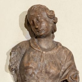 Zdjęcie nr 1: Przyścienna rzeźba ukazująca frontalnie młodą kobietę w całej postaci w kontrapoście umieszczona została na niskiej, czworobocznej podstawie. Postać ma lekko pochyloną głowę w lewo. Otaczają je falujące włosy spływające na plecy. Nie zachowały się ręce, które zostały ubite. Jej owalną twarz charakteryzuje wydatny nos oraz usta o pełnych wargach, a także spojrzenie skierowane w dół. Kobieta ubrana jest w zwiewną suknię przewiązaną w pasie wstążką. U dołu widać fragmenty bosych stóp. 