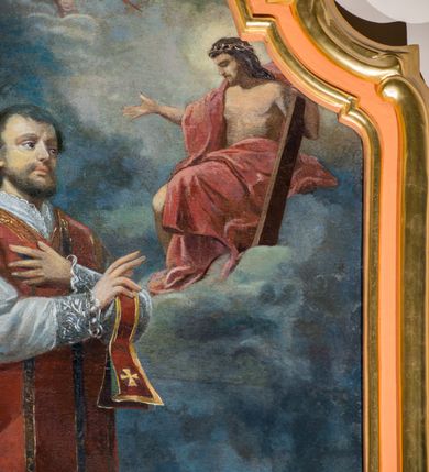 Zdjęcie nr 5: Obraz w kształcie stojącego prostokąta zamkniętego łukiem nadwieszonym z uskokiem. W centrum kompozycji stoi przedstawiony w całej postaci św. Walenty, który spogląda na ukazującego mu się Jezusa, lewą rękę składa na piersi, a prawą wyciąga w geście błogosławieństwa. Ma małą, owalną twarz, z głęboko osadzonymi oczami i małymi ustami otoczonymi wąsami i krótką brodą; włosy krótkie. Jest ubrany w białą albę z pasem koronki na dole i u rękawów i czerwony, lamowany złotem ornat, spod którego wystaje fragment stuły, przez lewą rękę ma przewiązany manipularz. Przed nim, na obłokach tronuje Chrystus ubrany jedynie w czerwony płaszcz. Prawą rękę wyciąga przed siebie, w lewej trzyma widoczny jedynie we fragmencie krzyż, spogląda na świętego. Z lewej strony kompozycji w stronę Walentego zlatuje putto trzymające wieniec z liści laurowych oraz palmę męczeństwa. W łuku zamykającym od góry kompozycję widoczne są dwa kolejne aniołki. U stóp Walentego, na ziemi leży kobieta w białej sukni z owiniętą głową. Jest przykryta czerwonym płaszczem, rękę składa na piersi, ma zamknięte oczy. W tle górzysty krajobraz, powyżej granatowe niebo, rozjaśnione jedynie za postacią Chrystusa. Obraz w złoconej, profilowanej ramie. 