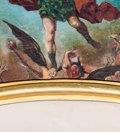 Zdjęcie nr 3: Obraz z przedstawieniem Michała Archanioła walczącego z szatanem. W centrum kompozycji archanioł w momencie ataku unosi się powyżej szatana na rozpostartych skrzydłach. W prawej ręce trzyma skierowany ostrzem w górę ognisty miecz, lewą unosi do boku. Archanioł ma małą, okrągłą głowę, długie, falowane włosy spływają mu na plecy. Jest ubrany w strój żołnierza rzymskiego: złoty pancerz z naramiennikami założony na zieloną tunikę i sandały. Czerwony płaszcz zarzucony na lewe ramię rozwiewa się dynamicznymi za plecami. W dolnej partii obrazu szatan zobrazowany jako człowiek z rogami i skrzydłami, uchyla się przed nadchodzącym ciosem. W prawym, dolnym rogu widać zielonego stwora z otwartym dziobem i rozpostartymi pazurami, w lewym wyciągniętą dłoń. Tło utrzymane w chłodnej, niebieskiej tonacji, ciemnieje w dolnej partii obrazu.  Obraz w złoconej, profilowanej ramie o wklęsło-wypukłym kształcie. 