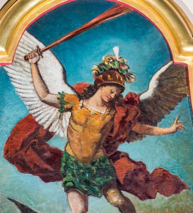 Zdjęcie nr 2: Obraz z przedstawieniem Michała Archanioła walczącego z szatanem. W centrum kompozycji archanioł w momencie ataku unosi się powyżej szatana na rozpostartych skrzydłach. W prawej ręce trzyma skierowany ostrzem w górę ognisty miecz, lewą unosi do boku. Archanioł ma małą, okrągłą głowę, długie, falowane włosy spływają mu na plecy. Jest ubrany w strój żołnierza rzymskiego: złoty pancerz z naramiennikami założony na zieloną tunikę i sandały. Czerwony płaszcz zarzucony na lewe ramię rozwiewa się dynamicznymi za plecami. W dolnej partii obrazu szatan zobrazowany jako człowiek z rogami i skrzydłami, uchyla się przed nadchodzącym ciosem. W prawym, dolnym rogu widać zielonego stwora z otwartym dziobem i rozpostartymi pazurami, w lewym wyciągniętą dłoń. Tło utrzymane w chłodnej, niebieskiej tonacji, ciemnieje w dolnej partii obrazu.  Obraz w złoconej, profilowanej ramie o wklęsło-wypukłym kształcie. 