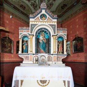 Zdjęcie nr 1: Ołtarz architektoniczny, przyścienny, jednokondygnacyjny, trójosiowy, ze zwieńczeniem. Ołtarz prostopadłościenny z antepedium zdobionym polichromowanym motywem liści akantu po bokach, pośrodku medalion z monogramem chrystologicznym. Tabernakulum w formie prostopadłościennej szafki z drzwiczkami zamkniętymi łukiem półkolistym ujętym fryzem arkadkowym, zdobionych monogramem chrystologicznym. Retabulum na niewysokim, zryzalitowanym cokole o zakończeniach w formie konsoli. Osi głównej części nastawy są w formie półkolistych arkad z niszami, wspartych parami kolumn o kapitelach kompozytowych, przy czym środkowa jest większa względem bocznych dźwigających belkowanie. Zwieńczenie części środkowej retabulum przybiera formę zbliżoną do trójkątnego przyczółka. Pola cokołu retabulum zdobi polichromowana i płaskorzeźbiona ornamentyka roślinna. Ścianki niszy pokryte są dekoracją malarską naśladującą wzorzyste tkaniny, a w górnej partii błękitne, gwieździste niebo. Łuki nisz ujmuje ażurowy fryz arkadkowy, dodatkowo obramienie niszy głównej z motywem rozetek. W przyłuczach dekoracja w formie wici roślinnej. Krawędź attyki oraz zwieńczenia zdobi ażurowa wić roślinna. W polu części środkowej znajduje się figura Madonny z Dzieciątkiem, w arkadzie po prawej stronie ołtarza św. Andrzeja, po lewej św. Piotra. Struktura ołtarza utrzymana jest w kolorach białym, niebieskim, zielonym i jasnoczerwonym, detal architektoniczny i ornamentyka są złocone.        