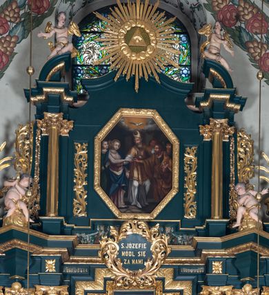 Zdjęcie nr 2: Nastawa architektoniczna, trójosiowa, dwukondygnacyjna, ustawiona na wysokim cokole z wyodrębnionymi prostopadłościanami. Ołtarz prostopadłościenny, z drewnianą mensą. Antepedium ujęte profilowaną ramą, w polu medalion z monogramem IHS w glorii. Na ołtarzu ustawione tabernakulum z tronem wystawienia. Tabernakulum w formie trójosiowej skrzynki, o wklęsło-wypukłym licu, artykułowanej kolumienkami o kręconych trzonach, podtrzymującymi belkowanie, wyłamane na ich osi, z gzymsem wyłamanym faliście na osi środkowej. Drzwiczki w formie stojącego prostokąta zamkniętego łukiem półkolistym nadwieszonym z uskokiem, ujętego ramą z płaskorzeźbionym przedstawieniem kielicha z hostią w glorii. Na osiach bocznych płaskorzeźbione przedstawienia winnego grona. Tron wystawienia w formie paludamentu, podwójnie podwieszonego po bokach, zwieńczonego koroną zamkniętą. 
Cokół dekorowany płycinami wypełnionymi suchym akantem. Pierwsza kondygnacja nastawy ujęta dwiema parami kolumn o kapitelach kompozytowych oraz stojącą między nimi parą pilastrów, w których trzonach znajdują się gabloty na wota. Przed pilastrami na cokołach ustawione dwie figury aniołów. Podpory dźwigają pełne belkowanie, przerwane w partii architrawu i fryzu nad polem środkowym, wyłamane na osi kolumn, na osi pilastrów belkowanie wyłamane pod kątem, w formie impostu z podwieszonymi szyszkami. Na belkowaniu, na obłokach dwie figurki adorujących puttów oraz dwa wazony na cokołach. W polu środkowym wnęka w formie stojącego prostokąta o wciętych górnych narożach, ujęta podwójną ramą, dekorowaną ornamentem roślinnym, z obrazem św. Józefa. Wnęka otoczona z trzech stron gablotami z wotami. Nad nią, w polu belkowania kartusz utworzony z suchego akantu z napisem w polu: „ŚW(IĘTY) JÓZEFIE / MÓDL SIĘ / ZA NAMI”. Druga kondygnacja o szerokości osi środkowej, ustawiona na cokole z wyodrębnionymi prostopadłościanami oraz gablotą z wotami, ujęta dwiema parami pilastrów i spływami wolutowymi oraz stojącą przed nimi parą kolumn, dźwigających zdwojone imposty oraz fragmenty przerwanego, półkolistego przyczółka z siedzącymi puttami. Spływy zdobione festonami utworzonymi z wstęgi oraz kwiatów. Całość zamknięta fragmentem falistego gzymsu oraz Okiem Opatrzności w glorii promienistej. W polu obraz Zaślubin Marii ze św. Józefem w formie stojącego prostokąta o ściętych narożach, ujęty ramą dekorowaną ornamentem roślinnym. Flankowany dwiema prostokątnymi płycinami wypełnionymi akantem. Obie kondygnacje ujęte uszami utworzonymi z suchego akantu. Struktura polichromowana w kolorze zielonym, kolumny, ornamentyka i profile złocone.




