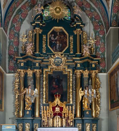 Zdjęcie nr 1: Nastawa architektoniczna, trójosiowa, dwukondygnacyjna, ustawiona na wysokim cokole z wyodrębnionymi prostopadłościanami. Ołtarz prostopadłościenny, z drewnianą mensą. Antepedium ujęte profilowaną ramą, w polu medalion z monogramem IHS w glorii. Na ołtarzu ustawione tabernakulum z tronem wystawienia. Tabernakulum w formie trójosiowej skrzynki, o wklęsło-wypukłym licu, artykułowanej kolumienkami o kręconych trzonach, podtrzymującymi belkowanie, wyłamane na ich osi, z gzymsem wyłamanym faliście na osi środkowej. Drzwiczki w formie stojącego prostokąta zamkniętego łukiem półkolistym nadwieszonym z uskokiem, ujętego ramą z płaskorzeźbionym przedstawieniem kielicha z hostią w glorii. Na osiach bocznych płaskorzeźbione przedstawienia winnego grona. Tron wystawienia w formie paludamentu, podwójnie podwieszonego po bokach, zwieńczonego koroną zamkniętą. 
Cokół dekorowany płycinami wypełnionymi suchym akantem. Pierwsza kondygnacja nastawy ujęta dwiema parami kolumn o kapitelach kompozytowych oraz stojącą między nimi parą pilastrów, w których trzonach znajdują się gabloty na wota. Przed pilastrami na cokołach ustawione dwie figury aniołów. Podpory dźwigają pełne belkowanie, przerwane w partii architrawu i fryzu nad polem środkowym, wyłamane na osi kolumn, na osi pilastrów belkowanie wyłamane pod kątem, w formie impostu z podwieszonymi szyszkami. Na belkowaniu, na obłokach dwie figurki adorujących puttów oraz dwa wazony na cokołach. W polu środkowym wnęka w formie stojącego prostokąta o wciętych górnych narożach, ujęta podwójną ramą, dekorowaną ornamentem roślinnym, z obrazem św. Józefa. Wnęka otoczona z trzech stron gablotami z wotami. Nad nią, w polu belkowania kartusz utworzony z suchego akantu z napisem w polu: „ŚW(IĘTY) JÓZEFIE / MÓDL SIĘ / ZA NAMI”. Druga kondygnacja o szerokości osi środkowej, ustawiona na cokole z wyodrębnionymi prostopadłościanami oraz gablotą z wotami, ujęta dwiema parami pilastrów i spływami wolutowymi oraz stojącą przed nimi parą kolumn, dźwigających zdwojone imposty oraz fragmenty przerwanego, półkolistego przyczółka z siedzącymi puttami. Spływy zdobione festonami utworzonymi z wstęgi oraz kwiatów. Całość zamknięta fragmentem falistego gzymsu oraz Okiem Opatrzności w glorii promienistej. W polu obraz Zaślubin Marii ze św. Józefem w formie stojącego prostokąta o ściętych narożach, ujęty ramą dekorowaną ornamentem roślinnym. Flankowany dwiema prostokątnymi płycinami wypełnionymi akantem. Obie kondygnacje ujęte uszami utworzonymi z suchego akantu. Struktura polichromowana w kolorze zielonym, kolumny, ornamentyka i profile złocone.




