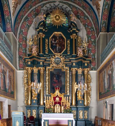 Zdjęcie nr 4: Nastawa architektoniczna, trójosiowa, dwukondygnacyjna, ustawiona na wysokim cokole z wyodrębnionymi prostopadłościanami. Ołtarz prostopadłościenny, z drewnianą mensą. Antepedium ujęte profilowaną ramą, w polu medalion z monogramem IHS w glorii. Na ołtarzu ustawione tabernakulum z tronem wystawienia. Tabernakulum w formie trójosiowej skrzynki, o wklęsło-wypukłym licu, artykułowanej kolumienkami o kręconych trzonach, podtrzymującymi belkowanie, wyłamane na ich osi, z gzymsem wyłamanym faliście na osi środkowej. Drzwiczki w formie stojącego prostokąta zamkniętego łukiem półkolistym nadwieszonym z uskokiem, ujętego ramą z płaskorzeźbionym przedstawieniem kielicha z hostią w glorii. Na osiach bocznych płaskorzeźbione przedstawienia winnego grona. Tron wystawienia w formie paludamentu, podwójnie podwieszonego po bokach, zwieńczonego koroną zamkniętą. 
Cokół dekorowany płycinami wypełnionymi suchym akantem. Pierwsza kondygnacja nastawy ujęta dwiema parami kolumn o kapitelach kompozytowych oraz stojącą między nimi parą pilastrów, w których trzonach znajdują się gabloty na wota. Przed pilastrami na cokołach ustawione dwie figury aniołów. Podpory dźwigają pełne belkowanie, przerwane w partii architrawu i fryzu nad polem środkowym, wyłamane na osi kolumn, na osi pilastrów belkowanie wyłamane pod kątem, w formie impostu z podwieszonymi szyszkami. Na belkowaniu, na obłokach dwie figurki adorujących puttów oraz dwa wazony na cokołach. W polu środkowym wnęka w formie stojącego prostokąta o wciętych górnych narożach, ujęta podwójną ramą, dekorowaną ornamentem roślinnym, z obrazem św. Józefa. Wnęka otoczona z trzech stron gablotami z wotami. Nad nią, w polu belkowania kartusz utworzony z suchego akantu z napisem w polu: „ŚW(IĘTY) JÓZEFIE / MÓDL SIĘ / ZA NAMI”. Druga kondygnacja o szerokości osi środkowej, ustawiona na cokole z wyodrębnionymi prostopadłościanami oraz gablotą z wotami, ujęta dwiema parami pilastrów i spływami wolutowymi oraz stojącą przed nimi parą kolumn, dźwigających zdwojone imposty oraz fragmenty przerwanego, półkolistego przyczółka z siedzącymi puttami. Spływy zdobione festonami utworzonymi z wstęgi oraz kwiatów. Całość zamknięta fragmentem falistego gzymsu oraz Okiem Opatrzności w glorii promienistej. W polu obraz Zaślubin Marii ze św. Józefem w formie stojącego prostokąta o ściętych narożach, ujęty ramą dekorowaną ornamentem roślinnym. Flankowany dwiema prostokątnymi płycinami wypełnionymi akantem. Obie kondygnacje ujęte uszami utworzonymi z suchego akantu. Struktura polichromowana w kolorze zielonym, kolumny, ornamentyka i profile złocone.




