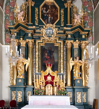Zdjęcie nr 5: Nastawa architektoniczna, trójosiowa, dwukondygnacyjna, ustawiona na wysokim cokole z wyodrębnionymi prostopadłościanami. Ołtarz prostopadłościenny, z drewnianą mensą. Antepedium ujęte profilowaną ramą, w polu medalion z monogramem IHS w glorii. Na ołtarzu ustawione tabernakulum z tronem wystawienia. Tabernakulum w formie trójosiowej skrzynki, o wklęsło-wypukłym licu, artykułowanej kolumienkami o kręconych trzonach, podtrzymującymi belkowanie, wyłamane na ich osi, z gzymsem wyłamanym faliście na osi środkowej. Drzwiczki w formie stojącego prostokąta zamkniętego łukiem półkolistym nadwieszonym z uskokiem, ujętego ramą z płaskorzeźbionym przedstawieniem kielicha z hostią w glorii. Na osiach bocznych płaskorzeźbione przedstawienia winnego grona. Tron wystawienia w formie paludamentu, podwójnie podwieszonego po bokach, zwieńczonego koroną zamkniętą. 
Cokół dekorowany płycinami wypełnionymi suchym akantem. Pierwsza kondygnacja nastawy ujęta dwiema parami kolumn o kapitelach kompozytowych oraz stojącą między nimi parą pilastrów, w których trzonach znajdują się gabloty na wota. Przed pilastrami na cokołach ustawione dwie figury aniołów. Podpory dźwigają pełne belkowanie, przerwane w partii architrawu i fryzu nad polem środkowym, wyłamane na osi kolumn, na osi pilastrów belkowanie wyłamane pod kątem, w formie impostu z podwieszonymi szyszkami. Na belkowaniu, na obłokach dwie figurki adorujących puttów oraz dwa wazony na cokołach. W polu środkowym wnęka w formie stojącego prostokąta o wciętych górnych narożach, ujęta podwójną ramą, dekorowaną ornamentem roślinnym, z obrazem św. Józefa. Wnęka otoczona z trzech stron gablotami z wotami. Nad nią, w polu belkowania kartusz utworzony z suchego akantu z napisem w polu: „ŚW(IĘTY) JÓZEFIE / MÓDL SIĘ / ZA NAMI”. Druga kondygnacja o szerokości osi środkowej, ustawiona na cokole z wyodrębnionymi prostopadłościanami oraz gablotą z wotami, ujęta dwiema parami pilastrów i spływami wolutowymi oraz stojącą przed nimi parą kolumn, dźwigających zdwojone imposty oraz fragmenty przerwanego, półkolistego przyczółka z siedzącymi puttami. Spływy zdobione festonami utworzonymi z wstęgi oraz kwiatów. Całość zamknięta fragmentem falistego gzymsu oraz Okiem Opatrzności w glorii promienistej. W polu obraz Zaślubin Marii ze św. Józefem w formie stojącego prostokąta o ściętych narożach, ujęty ramą dekorowaną ornamentem roślinnym. Flankowany dwiema prostokątnymi płycinami wypełnionymi akantem. Obie kondygnacje ujęte uszami utworzonymi z suchego akantu. Struktura polichromowana w kolorze zielonym, kolumny, ornamentyka i profile złocone.





