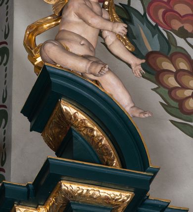 Zdjęcie nr 28: Nastawa architektoniczna, trójosiowa, dwukondygnacyjna, ustawiona na wysokim cokole z wyodrębnionymi prostopadłościanami. Ołtarz prostopadłościenny, z drewnianą mensą. Antepedium ujęte profilowaną ramą, w polu medalion z monogramem IHS w glorii. Na ołtarzu ustawione tabernakulum z tronem wystawienia. Tabernakulum w formie trójosiowej skrzynki, o wklęsło-wypukłym licu, artykułowanej kolumienkami o kręconych trzonach, podtrzymującymi belkowanie, wyłamane na ich osi, z gzymsem wyłamanym faliście na osi środkowej. Drzwiczki w formie stojącego prostokąta zamkniętego łukiem półkolistym nadwieszonym z uskokiem, ujętego ramą z płaskorzeźbionym przedstawieniem kielicha z hostią w glorii. Na osiach bocznych płaskorzeźbione przedstawienia winnego grona. Tron wystawienia w formie paludamentu, podwójnie podwieszonego po bokach, zwieńczonego koroną zamkniętą. 
Cokół dekorowany płycinami wypełnionymi suchym akantem. Pierwsza kondygnacja nastawy ujęta dwiema parami kolumn o kapitelach kompozytowych oraz stojącą między nimi parą pilastrów, w których trzonach znajdują się gabloty na wota. Przed pilastrami na cokołach ustawione dwie figury aniołów. Podpory dźwigają pełne belkowanie, przerwane w partii architrawu i fryzu nad polem środkowym, wyłamane na osi kolumn, na osi pilastrów belkowanie wyłamane pod kątem, w formie impostu z podwieszonymi szyszkami. Na belkowaniu, na obłokach dwie figurki adorujących puttów oraz dwa wazony na cokołach. W polu środkowym wnęka w formie stojącego prostokąta o wciętych górnych narożach, ujęta podwójną ramą, dekorowaną ornamentem roślinnym, z obrazem św. Józefa. Wnęka otoczona z trzech stron gablotami z wotami. Nad nią, w polu belkowania kartusz utworzony z suchego akantu z napisem w polu: „ŚW(IĘTY) JÓZEFIE / MÓDL SIĘ / ZA NAMI”. Druga kondygnacja o szerokości osi środkowej, ustawiona na cokole z wyodrębnionymi prostopadłościanami oraz gablotą z wotami, ujęta dwiema parami pilastrów i spływami wolutowymi oraz stojącą przed nimi parą kolumn, dźwigających zdwojone imposty oraz fragmenty przerwanego, półkolistego przyczółka z siedzącymi puttami. Spływy zdobione festonami utworzonymi z wstęgi oraz kwiatów. Całość zamknięta fragmentem falistego gzymsu oraz Okiem Opatrzności w glorii promienistej. W polu obraz Zaślubin Marii ze św. Józefem w formie stojącego prostokąta o ściętych narożach, ujęty ramą dekorowaną ornamentem roślinnym. Flankowany dwiema prostokątnymi płycinami wypełnionymi akantem. Obie kondygnacje ujęte uszami utworzonymi z suchego akantu. Struktura polichromowana w kolorze zielonym, kolumny, ornamentyka i profile złocone.





