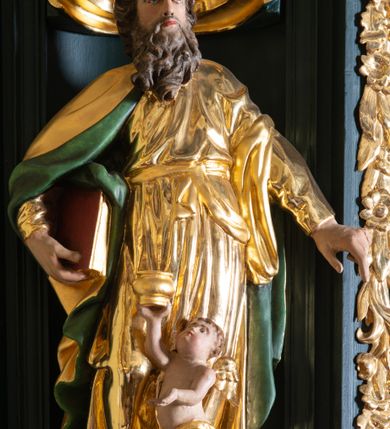 Zdjęcie nr 10: Ambona przyścienna, wisząca, z dostępem w formie jednobiegowych schodów. Kosz na planie ściętego ośmioboku, z podwieszeniem w formie spłaszczonego, ośmiobocznego wałka, zakończonego szyszką. Kosz na wysokim cokole, ścianki wydzielone pilastrami dekorowanymi muszlami i zwisami kwiatowymi, dźwigającymi pełne belkowanie z silnie wysuniętym gzymsem tworzącym parapet, dekorowanym ornamentem roślinnym. W polu ścianek nisze z konchami i figurami czterech ewangelistów, stojącymi na wspornikach. Balustrada schodów pełna, dekorowana płycinami wypełnionymi akantem, zakończona filarem z wazonem. Zaplecek zakończony gzymsem, ujęty uszami utworzonymi z suchego akantu. W polu płycina w formie stojącego prostokąta o wklęsłych narożach, w niej nisza z konchą, na tle której na wsporniku ustawiona figura Chrystusa. Baldachim na planie ściętego ośmioboku, w formie belkowania, wyłamanego na narożach. Na nim, na niskiej podstawie osiem kabłąków dekorowanych cokolikami z wazonami, podtrzymujących spłaszczoną kulę, na której stoi figura anioła z banderolą z napisem „KTO WAS SŁUCHA MNIE SŁUCHA”. Na podniebieniu baldachimu rzeźba gołębicy Ducha Świętego w glorii promienistej. Struktura polichromowana w kolorze zielonym, ze złoconymi profilami i ornamentyką. 

Figura anioła ukazana frontalnie, w kontrapoście, z głową skierowaną w lewo, obiema rękami trzyma banderolę. Twarz ma pociągłą, o migdałowatych oczach, dużym nosie i rozchylonych ustach, okoloną krótkimi, kręconymi, rozwianymi włosami. Anioł ubrany jest w długą, silnie drapowaną, złoconą tunikę, przepasaną w talii, odsłaniającą prawe ramię oraz obie nogi. Skrzydła ma złożone po bokach postaci. 

Figura Chrystusa ukazana frontalnie, w kontrapoście, prawą rękę unosi w geście błogosławieństwa, w lewej trzyma jabłko królewskie. Twarz ma szczupłą, o migdałowatych oczach, dużym nosie i wąskich ustach, okoloną brązową brodą i włosami sięgającymi ramion. Chrystus ubrany jest w przylegającą do ciała, złoconą tunikę, przepasaną w talii oraz złocony płaszcz o czerwonej podszewce, przerzucony diagonalnie przez lewe ramię. 

Figura św. Jana ukazana frontalnie, w kontrapoście, przechylona w lewo, prawą rękę wyciąga do przodu, lewą podtrzymuje otwartą księgę. Twarz ma owalną, o migdałowatych oczach, dużym nosie i wąskich ustach, okoloną brązowymi włosami sięgającymi ramion. Święty ubrany jest w przylegającą do ciała, złoconą tunikę, przepasaną w talii oraz złocony płaszcz o czerwonej podszewce, przerzucony diagonalnie przez lewe ramię, zawieszony na taśmie z przodu postaci. 

Figura św. Łukasza ukazana frontalnie, w kontrapoście, przechylona w lewo, prawą rękę unosi na tle piersi, lewą podtrzymuje otwartą księgę. Twarz ma owalną, o migdałowatych oczach, dużym nosie i wąskich ustach, okoloną brązową długą brodą i krótkimi włosami. Święty ubrany jest w przylegającą do ciała, złoconą tunikę, przepasaną w talii oraz złocony płaszcz o zielonej podszewce, przerzucony diagonalnie przez lewe ramię. Przy prawej nodze świętego głowa wołu. 

Figura św. Marka ukazana frontalnie, w kontrapoście, przechylona w lewo, z głową zwróconą w lewo, prawą rękę wyciąga w bok, lewą przytrzymuje przy boku księgę. Twarz ma owalną, o migdałowatych oczach, dużym nosie i wąskich ustach, okoloną gęstą, brązową brodą i krótkimi, kręconymi włosami. Święty ubrany jest w przylegającą do ciała, złoconą tunikę, przepasaną w talii oraz złocony płaszcz o jasnozielonej podszewce, zarzucony na ramiona i zawiązany z przodu. Przy lewej nodze postaci głowa lwa. 

Figura św. Mateusza ukazana frontalnie, w kontrapoście, lewą rękę wyciąga w bok, prawą przytrzymuje przy boku księgę. Twarz ma owalną, o migdałowatych oczach, dużym nosie i wąskich ustach, okoloną długą, brązową brodą i krótkimi włosami. Święty ubrany jest w przylegającą do ciała, złoconą tunikę, przepasaną w talii szarfą oraz złocony płaszcz o zielonej podszewce, zarzucony na ramiona i opadający po bokach. Przed świętym figurka aniołka trzymającego miskę. 
