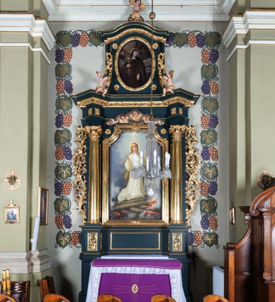 Zdjęcie nr 1: Nastawa architektoniczna, jednoosiowa, jednokondygnacyjna ze zwieńczeniem, ustawiona na dwustrefowym cokole z wyodrębnionymi dwoma prostopadłościanami. Ołtarz prostopadłościenny, z drewnianą mensą. Antepedium ujęte profilowaną, złoconą ramą, na tle fioletowego pola mandorla z chrystogramem Chi Rho oraz literami alfa i omega, w glorii promienistej. Cokół w górnej strefie dekorowany płycinami wypełnionymi akantem. Nastawa flankowana parą kolumn o kapitelach kompozytowych, dźwigających pełne belkowanie, wyłamane pod kątem na ich osi, przerwane pośrodku, z siedzącymi na nim puttami, o fryzie dekorowanym rozetami. Pole centralne niemal w całości wypełnione wnęką ujętą profilowaną ramą zdobioną miejscami  ornamentem roślinnym, w formie stojącego prostokąta o wklęsłych górnych narożach. We wnęce obraz z przedstawieniem św. Agnieszki, na zasuwie św. Bonawentury i św. Tomasza z Akwinu. Nad obrazem rzeźbione obłoki z trzema uskrzydlonymi główkami anielskimi. Kondygnacja ujęta uszami utworzonymi z akantu i kampanuli. Zwieńczenie w formie stojącego prostokąta o lekko wklęsłych bokach, zamknięte fragmentem falistego gzymsu, na którym siedzi putto. W polu obraz św. Klary w formie stojącego owalu, ujęty ramą zdobioną wieńcem laurowym. Zwieńczenie dekorowane w polu czterema rozetami, flankowane uszami z akantu. Struktura polichromowana w kolorze zielonym, ze złoconymi kolumnami, profilami i ornamentyką. 