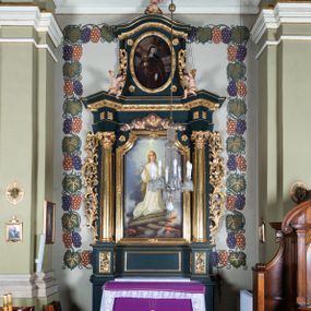 Zdjęcie nr 1: Nastawa architektoniczna, jednoosiowa, jednokondygnacyjna ze zwieńczeniem, ustawiona na dwustrefowym cokole z wyodrębnionymi dwoma prostopadłościanami. Ołtarz prostopadłościenny, z drewnianą mensą. Antepedium ujęte profilowaną, złoconą ramą, na tle fioletowego pola mandorla z chrystogramem Chi Rho oraz literami alfa i omega, w glorii promienistej. Cokół w górnej strefie dekorowany płycinami wypełnionymi akantem. Nastawa flankowana parą kolumn o kapitelach kompozytowych, dźwigających pełne belkowanie, wyłamane pod kątem na ich osi, przerwane pośrodku, z siedzącymi na nim puttami, o fryzie dekorowanym rozetami. Pole centralne niemal w całości wypełnione wnęką ujętą profilowaną ramą zdobioną miejscami  ornamentem roślinnym, w formie stojącego prostokąta o wklęsłych górnych narożach. We wnęce obraz z przedstawieniem św. Agnieszki, na zasuwie św. Bonawentury i św. Tomasza z Akwinu. Nad obrazem rzeźbione obłoki z trzema uskrzydlonymi główkami anielskimi. Kondygnacja ujęta uszami utworzonymi z akantu i kampanuli. Zwieńczenie w formie stojącego prostokąta o lekko wklęsłych bokach, zamknięte fragmentem falistego gzymsu, na którym siedzi putto. W polu obraz św. Klary w formie stojącego owalu, ujęty ramą zdobioną wieńcem laurowym. Zwieńczenie dekorowane w polu czterema rozetami, flankowane uszami z akantu. Struktura polichromowana w kolorze zielonym, ze złoconymi kolumnami, profilami i ornamentyką. 