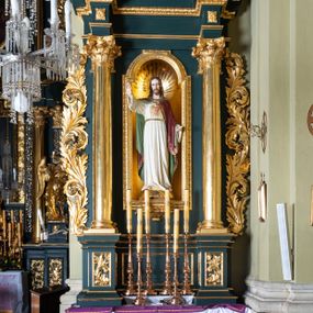 Zdjęcie nr 1: Nastawa architektoniczna, jednoosiowa, dwukondygnacyjna, ustawiona na cokole z wyodrębnionymi dwoma prostopadłościanami. Ołtarz prostopadłościenny, z drewnianą mensą. Antepedium ujęte profilowaną ramą, w polu medalion z monogramem IHS w glorii. Cokół dekorowany płycinami w partii wyodrębnionych prostopadłościanów wypełnionymi akantem. Pierwsza kondygnacja flankowana parą pilastrów i stojących przed nimi kolumn o kapitelach kompozytowych, dźwigających pełne belkowanie, wyłamane na ich osi, o fryzie dekorowanym rozetami. W polu centralnym nisza w formie stojącego prostokąta, zamkniętego łukiem półkolistym nadwieszonym, ujęta ramą zdobioną ornamentem roślinnym, z figurą Najświętszego Serca Jezusa. Druga kondygnacja ustawiona na cokole z wyodrębnionymi prostopadłościanami, flankowana parą pilastrów i stojących przed nimi kolumn o kapitelach kompozytowych, dźwigających imposty i fragmenty przerwanego, półkolistego przyczółka. Całość zamknięta fragmentem falistego gzymsu. W polu obraz św. Szymona z Lipnicy w formie stojącego prostokąta o ściętych narożach, ujętego ramą zdobioną ornamentem roślinnym. Obie kondygnacje z uszami utworzonymi ze stylizowanego akantu. Struktura polichromowana w kolorze zielonym, ze złoconymi kolumnami, profilami i ornamentyką. 