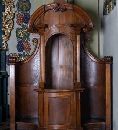 Zdjęcie nr 1: Konfesjonał na rzucie prostokąta z wklęsło-wypukłym frontem, lekko wklęsłymi zapleckami o ściankach ujętych spływami wolutowymi. Siedzisko z drzwiczkami lekko wybrzuszonymi, ujęte pilastrami z wybrzuszonym i profilowanym gzymsem oraz półkolistym przyczółkiem z dwiema stykającymi się wolutami.  