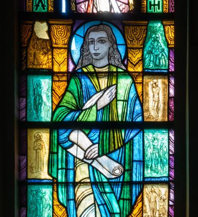 Zdjęcie nr 1: Witraż w kształcie stojącego prostokąta zamkniętego u góry łukiem półokrągłym. Kompozycja dwustrefowa. W dolnej części przedstawiony św. Jan Ewangelista ukazany frontalnie w ujęciu całopostaciowym. Święty wyobrażony jako młody mężczyzna o dużych, ciemnych oczach i długim, prostym nosie. Długie, falowane włosy opadają na ramiona postaci, skręcając się w spiralne loki. Postać ubrana w długą, jasnożółtą tunikę oraz płaszcz w odcieniach zieleni i błękitu trzymająca w prawej ręce pióro, w lewej zwój pergaminu. Spod szat widoczne bose stopy. W dolnej części kompozycji widoczny orzeł – symbol tego ewangelisty oraz banderola z napisem „EWANGELISTA ŚW(IĘTY) JAN”. W tle przedstawiono wąskie romańskie kolumny o roślinnych kapitelach i trzonach dekorowanych geometryczną plecionką. W prześwitach pomiędzy kolumnami wkomponowano mniejsze sceny ukazujące wydarzenia z życia Chrystusa opisane przez św. Jana. W górnej części kompozycji w arkadzie ujętej dwiema zdwojonymi kolumienkami ukazany błogosławiący Chrystus, przedstawiony w typie ikonograficznym Jezu Ufam Tobie. Postać ukazana frontalnie, w ujęciu całopostaciowym, ubrana w jasnobeżowe szaty. Wokół głowy Chrystusa nimb krzyżowy. W łuku arkady umieszczono napis: „MIŁOSIERDZIE BOŻE”, a w jej polu: „UFA/MY TO/BIE”. Arkada, w której umieszczono Zbawiciela, ujęta jest motywami roślinnymi oraz dwiema mniejszymi arkadkami mieszczącymi motyw litery Α i Ω oraz monogram w postaci litery H umieszczonej na tle krzyża. W arkadzie z lewej dodatkowo napis: „IN PRINCIPIO ERAT VERBUM” oraz „ET VERBUM CARO FACTUM EST”. W prawym, dolnym rogu witraża umieszczona jest sygnatura zakładu Żeleńskiego: „WYKONAŁ / S. G. ŻELE[ŃSKI] / KRAKÓW”.