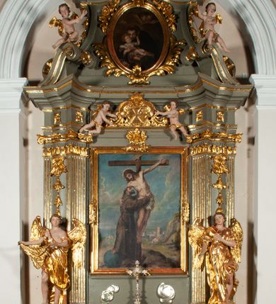 Zdjęcie nr 2: Ołtarz jednoosiowy, jednokondygnacyjny ze zwieńczeniem. Podwójny cokół z wąską, drewnianą mensą ołtarzową, tabernakulum ze spływami wolutowymi. Retabulum flankowane dwiema ćwierć kolumnami skierowanymi po ukosie na zewnątrz, z których każda ujęta parą korynckich, kanelowanych pilastrów dźwigających przełamujące się nad nimi belkowanie i dwa faliste naczółki. Na tle pilastrów, na konsolach stoją dwa uskrzydlone anioły. Zwieńczenie ujęte spływami wolutowymi, zakończone dwiema profilowanym, lekko falistym gzymsem z dwiema stykającymi się wolutami. W polu głównym szeroka, złocona, prostokątna rama z obrazami „Św. Mikołaj” i &quot;Wizja św. Franciszka&quot; na zasuwie, w zwieńczeniu owalny obraz w złoconej ramie z przedstawieniem św. Antoniego. Figury aniołów wydrążone, ukazane w kontrapoście, z dłońmi wysuniętymi do przodu; anioł po lewej trzyma chustę. Ich twarze są owalne o regularnych rysach, z brązowymi puklowanymi włosami sięgającymi ramion. Z tyłu przymocowane duże, złote skrzydła. Ubrane są w długie, złote szaty o ostrym zarysie, odsłaniające klatkę piersiową i jedną z nóg. W partii belkowania para nagich puttów ze złoconymi opaskami na biodrach ujmujących kartusz w rokokowym obramieniu z chrystogramem. Na naczółkach z kolei siedzą nagie putta z przepaskami na biodrach i złotymi skrzydełkami. Na dekorację ornamentalną składają się drobne motywy roślinne, kampanule na ćwierćkolumnach, zwisy róż i gałązek wokół obrazu w zwieńczeniu i efektowna podwójna muszla palmetowa w zwieńczeniu. 
