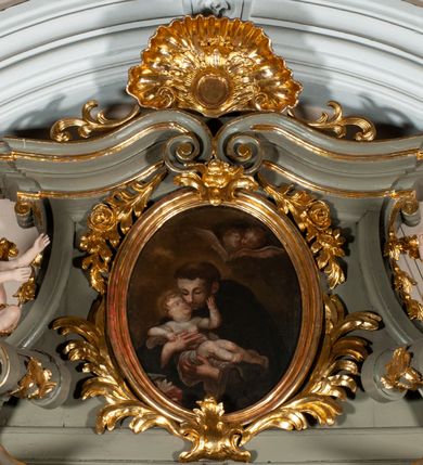 Zdjęcie nr 22: Ołtarz jednoosiowy, jednokondygnacyjny ze zwieńczeniem. Podwójny cokół z wąską, drewnianą mensą ołtarzową, tabernakulum ze spływami wolutowymi. Retabulum flankowane dwiema ćwierć kolumnami skierowanymi po ukosie na zewnątrz, z których każda ujęta parą korynckich, kanelowanych pilastrów dźwigających przełamujące się nad nimi belkowanie i dwa faliste naczółki. Na tle pilastrów, na konsolach stoją dwa uskrzydlone anioły. Zwieńczenie ujęte spływami wolutowymi, zakończone dwiema profilowanym, lekko falistym gzymsem z dwiema stykającymi się wolutami. W polu głównym szeroka, złocona, prostokątna rama z obrazami „Św. Mikołaj” i "Wizja św. Franciszka" na zasuwie, w zwieńczeniu owalny obraz w złoconej ramie z przedstawieniem św. Antoniego. Figury aniołów wydrążone, ukazane w kontrapoście, z dłońmi wysuniętymi do przodu; anioł po lewej trzyma chustę. Ich twarze są owalne o regularnych rysach, z brązowymi puklowanymi włosami sięgającymi ramion. Z tyłu przymocowane duże, złote skrzydła. Ubrane są w długie, złote szaty o ostrym zarysie, odsłaniające klatkę piersiową i jedną z nóg. W partii belkowania para nagich puttów ze złoconymi opaskami na biodrach ujmujących kartusz w rokokowym obramieniu z chrystogramem. Na naczółkach z kolei siedzą nagie putta z przepaskami na biodrach i złotymi skrzydełkami. Na dekorację ornamentalną składają się drobne motywy roślinne, kampanule na ćwierćkolumnach, zwisy róż i gałązek wokół obrazu w zwieńczeniu i efektowna podwójna muszla palmetowa w zwieńczeniu. 
