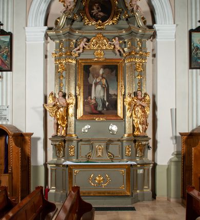 Zdjęcie nr 29: Ołtarz jednoosiowy, jednokondygnacyjny ze zwieńczeniem. Podwójny cokół z wąską, drewnianą mensą ołtarzową, tabernakulum ze spływami wolutowymi. Retabulum flankowane dwiema ćwierć kolumnami skierowanymi po ukosie na zewnątrz, z których każda ujęta parą korynckich, kanelowanych pilastrów dźwigających przełamujące się nad nimi belkowanie i dwa faliste naczółki. Na tle pilastrów, na konsolach stoją dwa uskrzydlone anioły. Zwieńczenie ujęte spływami wolutowymi, zakończone dwiema profilowanym, lekko falistym gzymsem z dwiema stykającymi się wolutami. W polu głównym szeroka, złocona, prostokątna rama z obrazami „Św. Mikołaj” i "Wizja św. Franciszka" na zasuwie, w zwieńczeniu owalny obraz w złoconej ramie z przedstawieniem św. Antoniego. Figury aniołów wydrążone, ukazane w kontrapoście, z dłońmi wysuniętymi do przodu; anioł po lewej trzyma chustę. Ich twarze są owalne o regularnych rysach, z brązowymi puklowanymi włosami sięgającymi ramion. Z tyłu przymocowane duże, złote skrzydła. Ubrane są w długie, złote szaty o ostrym zarysie, odsłaniające klatkę piersiową i jedną z nóg. W partii belkowania para nagich puttów ze złoconymi opaskami na biodrach ujmujących kartusz w rokokowym obramieniu z chrystogramem. Na naczółkach z kolei siedzą nagie putta z przepaskami na biodrach i złotymi skrzydełkami. Na dekorację ornamentalną składają się drobne motywy roślinne, kampanule na ćwierćkolumnach, zwisy róż i gałązek wokół obrazu w zwieńczeniu i efektowna podwójna muszla palmetowa w zwieńczeniu. 
