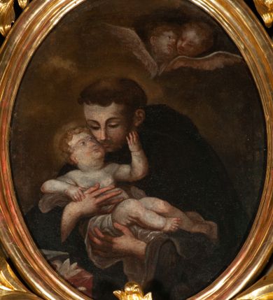 Zdjęcie nr 1: Obraz owalny z przedstawieniem św. Antoniego trzymającego na rękach nagiego Jezusa. Przed nim widoczny fragment nakrytego czerwoną tkaniną stolika z lilią i księgą, tło nieokreślone z parą główek anielskich. 