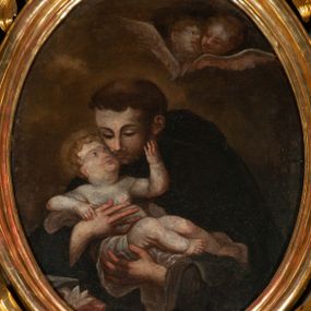 Zdjęcie nr 1: Obraz owalny z przedstawieniem św. Antoniego trzymającego na rękach nagiego Jezusa. Przed nim widoczny fragment nakrytego czerwoną tkaniną stolika z lilią i księgą, tło nieokreślone z parą główek anielskich. 