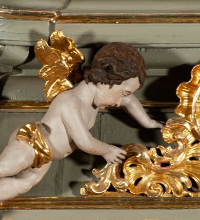 Zdjęcie nr 11: Ołtarz  jednoosiowy, jednokondygnacyjny ze zwieńczeniem. Podwójny cokół z wąską, drewnianą mensą ołtarzową, tabernakulum ze spływami wolutowymi. Retabulum flankowane dwiema ćwierć kolumnami skierowanymi po ukosie na zewnątrz, z których każda ujęta parą korynckich, kanelowanych pilastrów dźwigających przełamujące się nad nimi belkowanie i dwa faliste naczółki. Na tle pilastrów, na konsolach stoją dwa uskrzydlone anioły. Zwieńczenie ujęte spływami wolutowymi, zakończone profilowanym, lekko falistym gzymsem z dwiema stykającymi się wolutami. W polu głównym szeroka, złocona, prostokątna rama z obrazem "Św. Szymon Oracz", w zwieńczeniu owalny obraz w złoconej ramie z przedstawieniem św. Michała Archanioła. Figury aniołów wydrążone, ukazane w kontrapoście, o prawidłowych proporcjach ciała, w lekkim przechyleniu na bok, z dłońmi ułożonymi do gry na instrumencie szarpanym. Ich twarze są owalne o regularnych rysach, z brązowymi puklowanymi włosami sięgającymi ramion. Z tyłu przymocowane duże, złote skrzydła. Ubrani są w długie, złote szaty o ostrym zarysie. W partii belkowania para nagich puttów ze złoconymi opaskami na biodrach ujmują kartusz w rokokowym obramieniu. Na naczółkach z kolei siedzą nagie putta z przepaskami na biodrach i złotymi skrzydełkami. Na dekorację ornamentalną składają się drobne motywy roślinne, kampanule na ćwierćkolumnach, zwisy róż i gałązek wokół obrazu w zwieńczeniu i efektowna podwójna muszla palmetowa w zwieńczeniu. 



